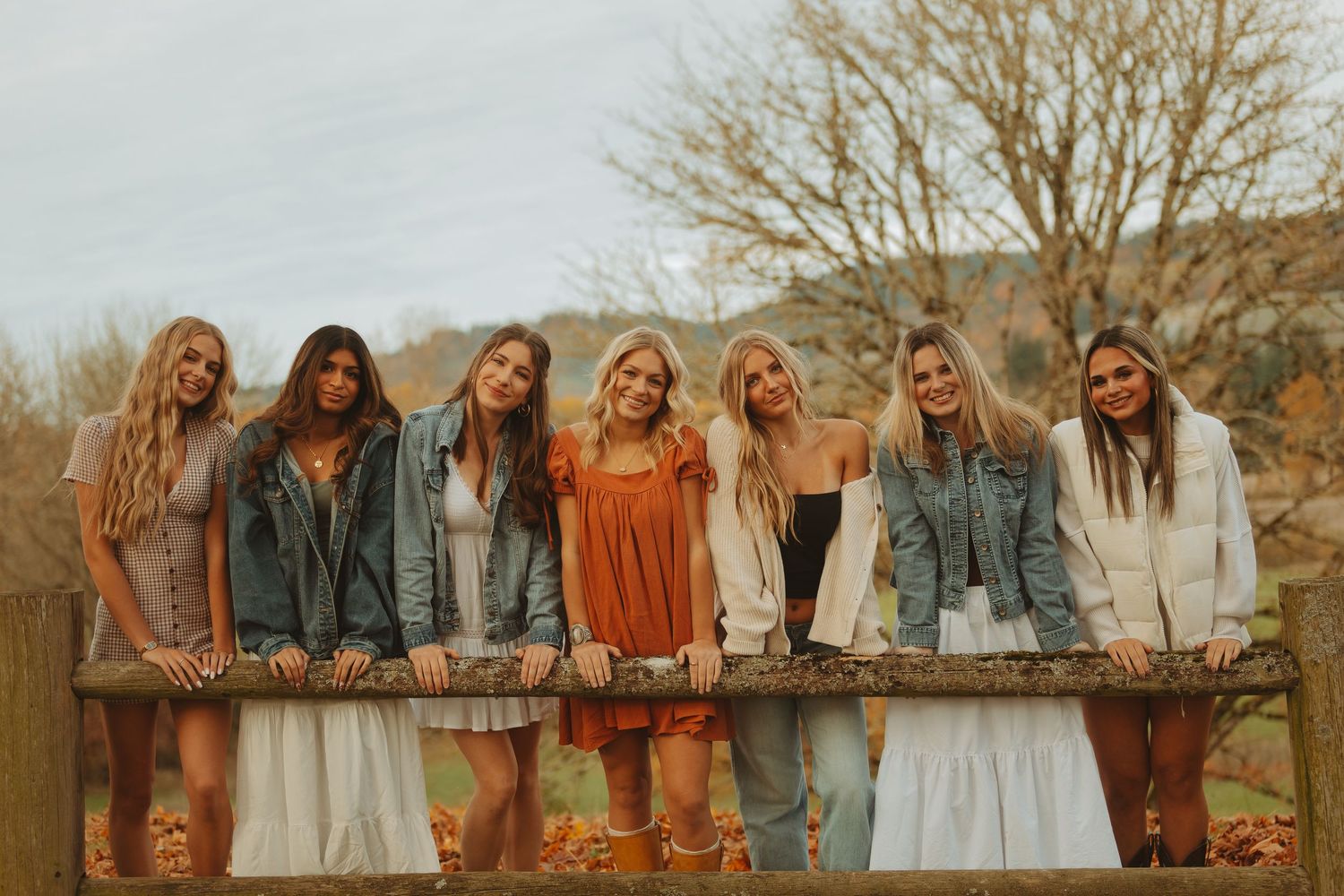 A group of people in coordinated outfits stand together outdoors in a line during autumn for a photo session.