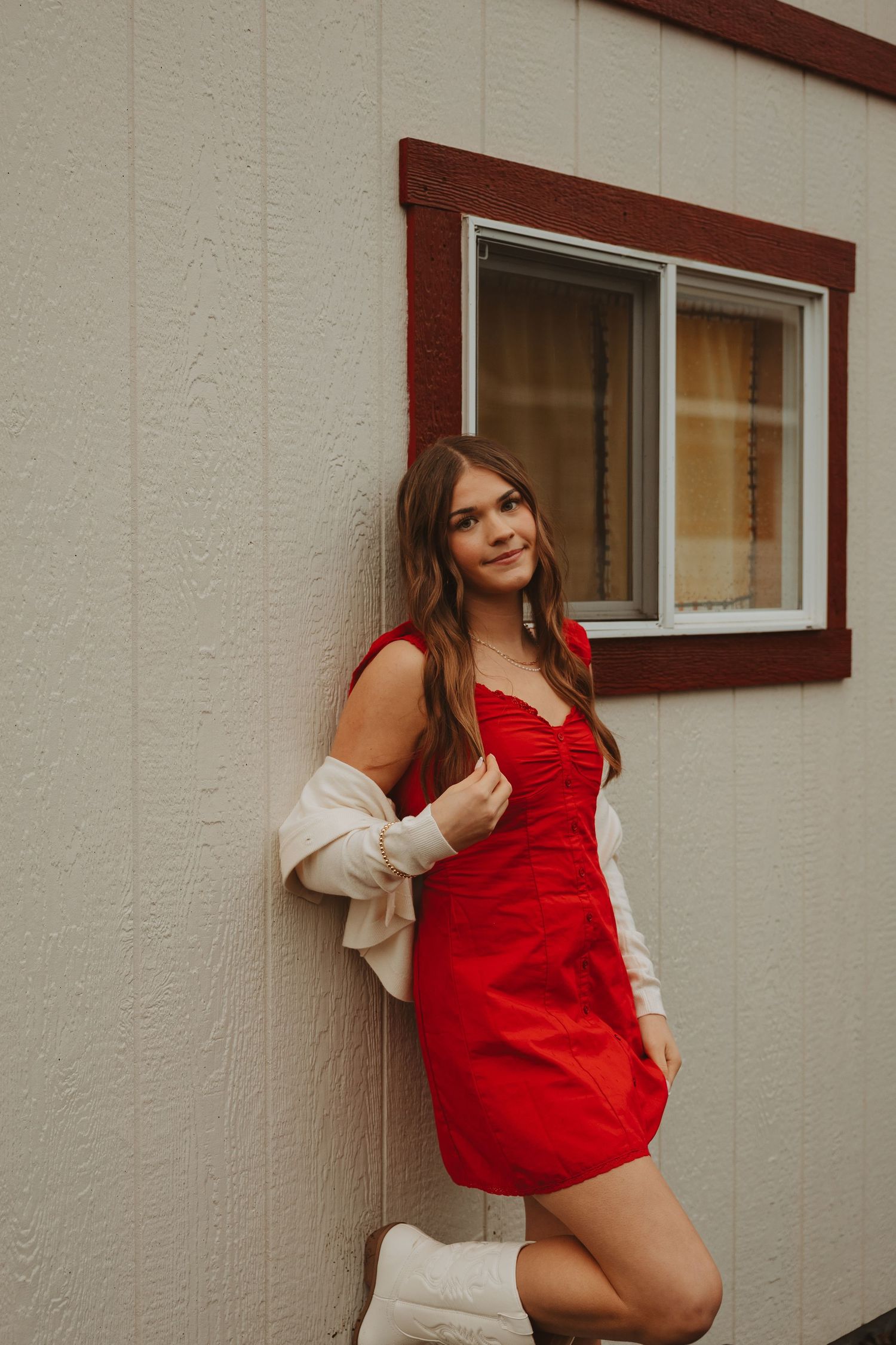 Fashion portrait in red dress and cream cardigan against white building exterior.