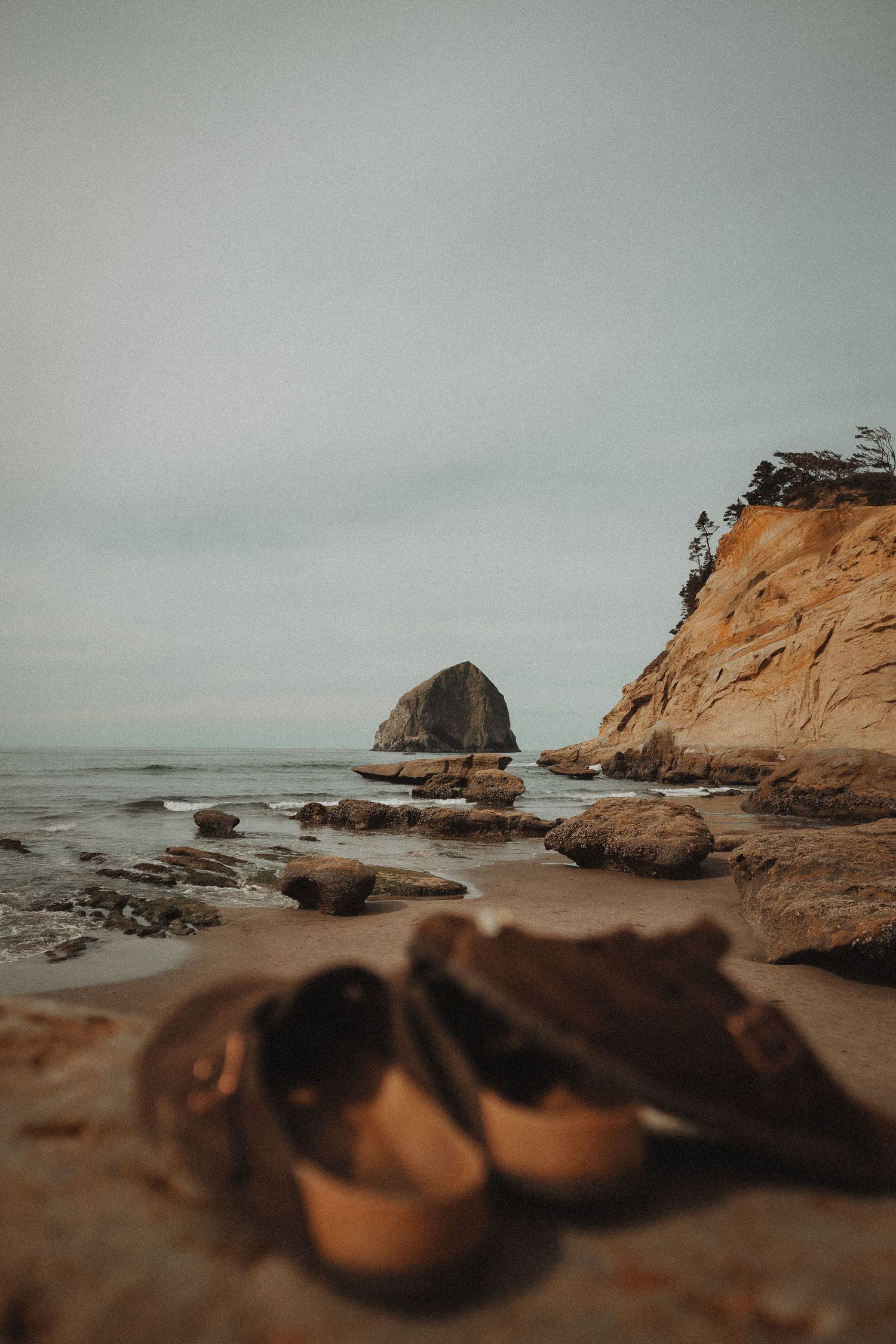Pair of shoes left on rocky beach with haystack rock and coastal cliffs in background.
