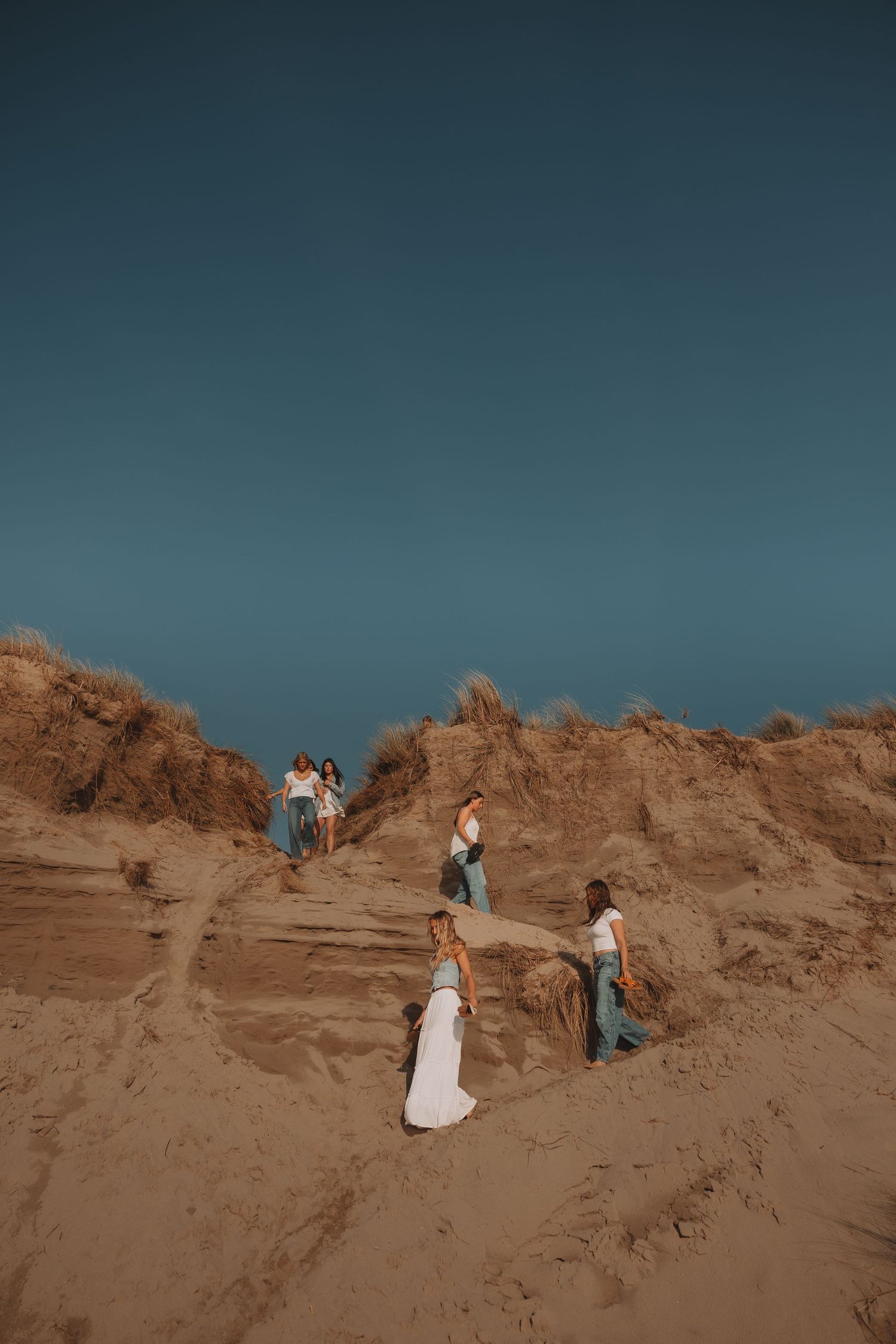 Group of women climbing sandy dunes under a clear blue sky in a desert landscape.