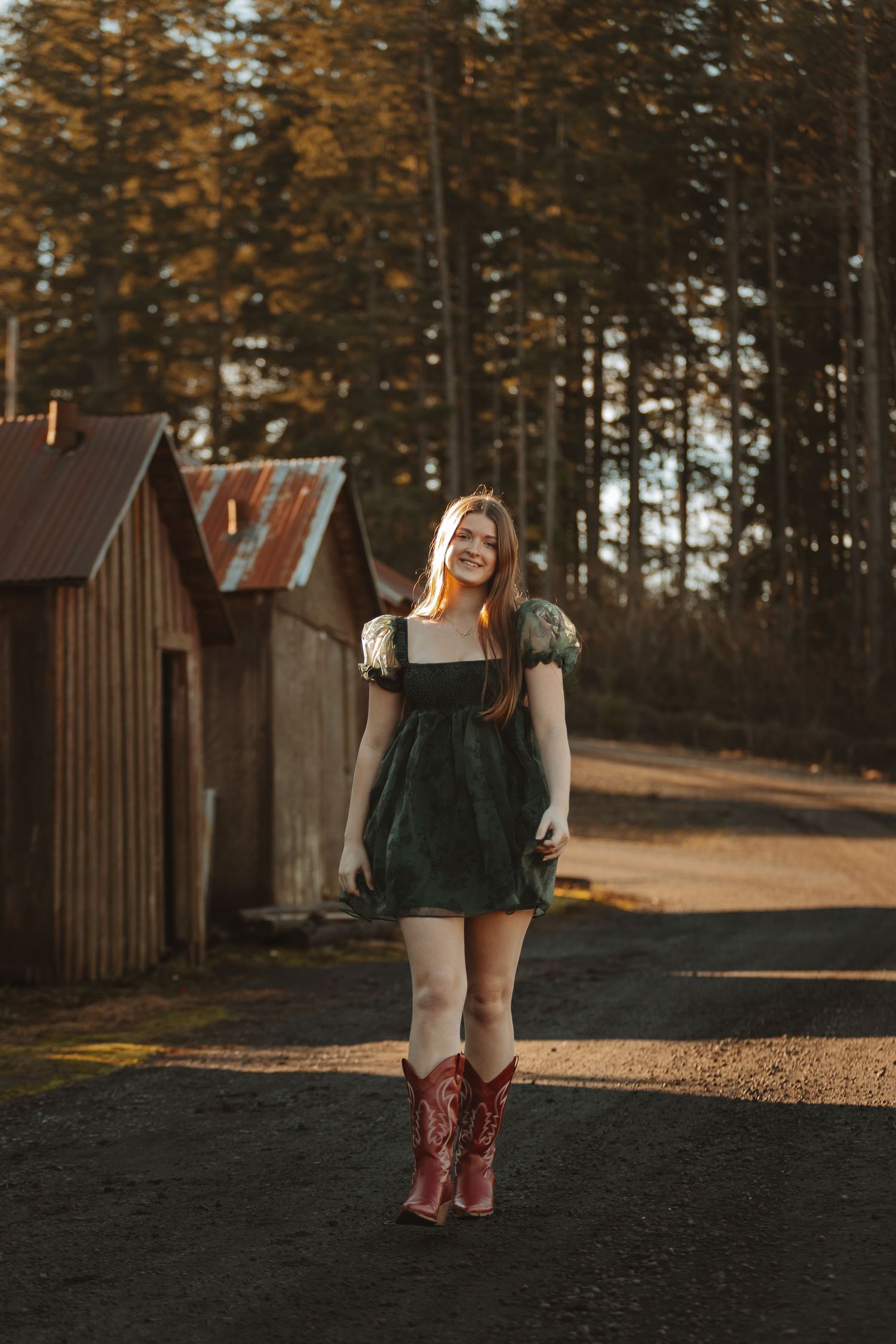 Person in dark dress and red boots poses playfully outside rustic cabins at sunset.