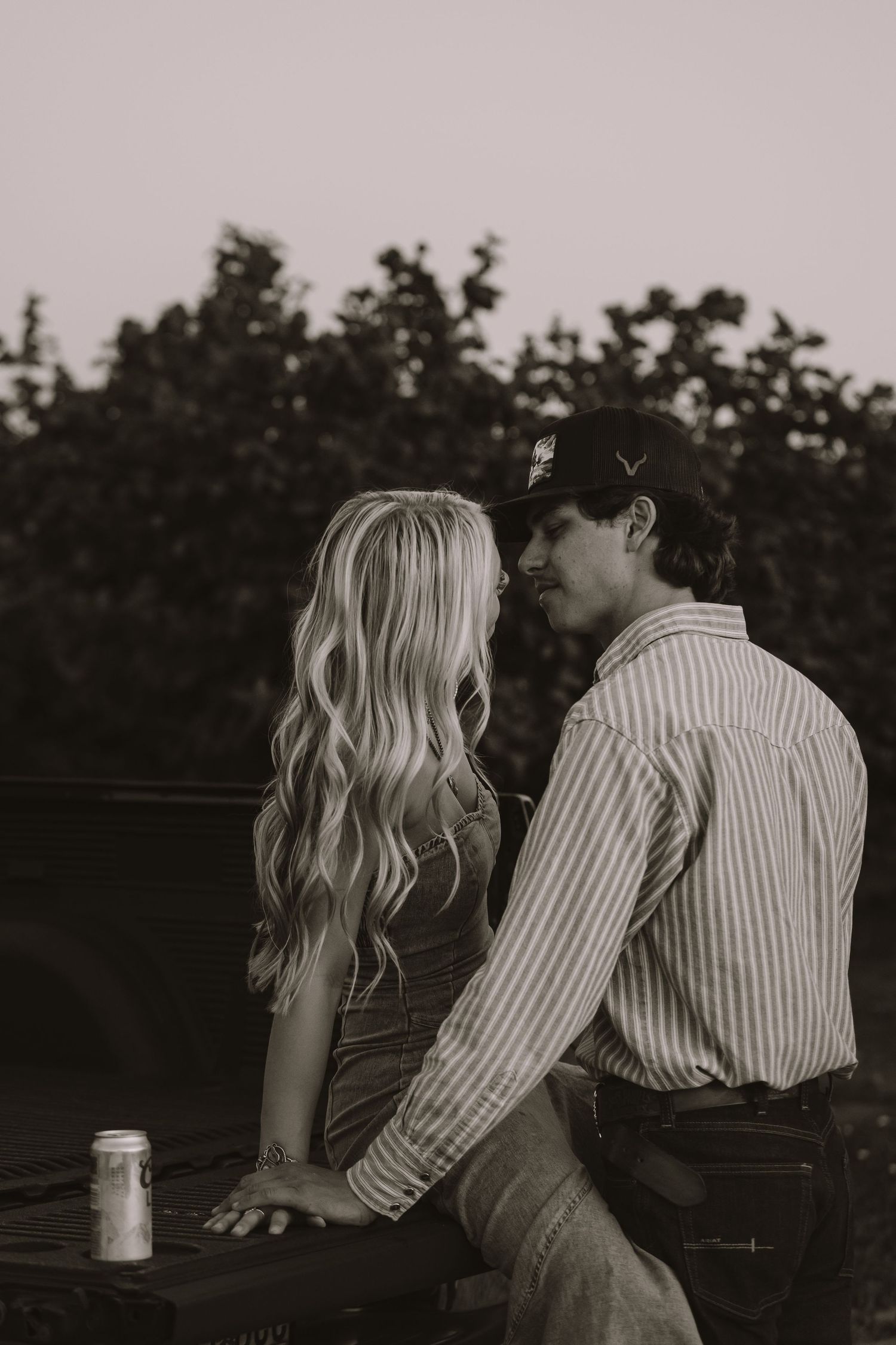 Black and white photo of a couple sitting close together on a truck tailgate at dusk.
