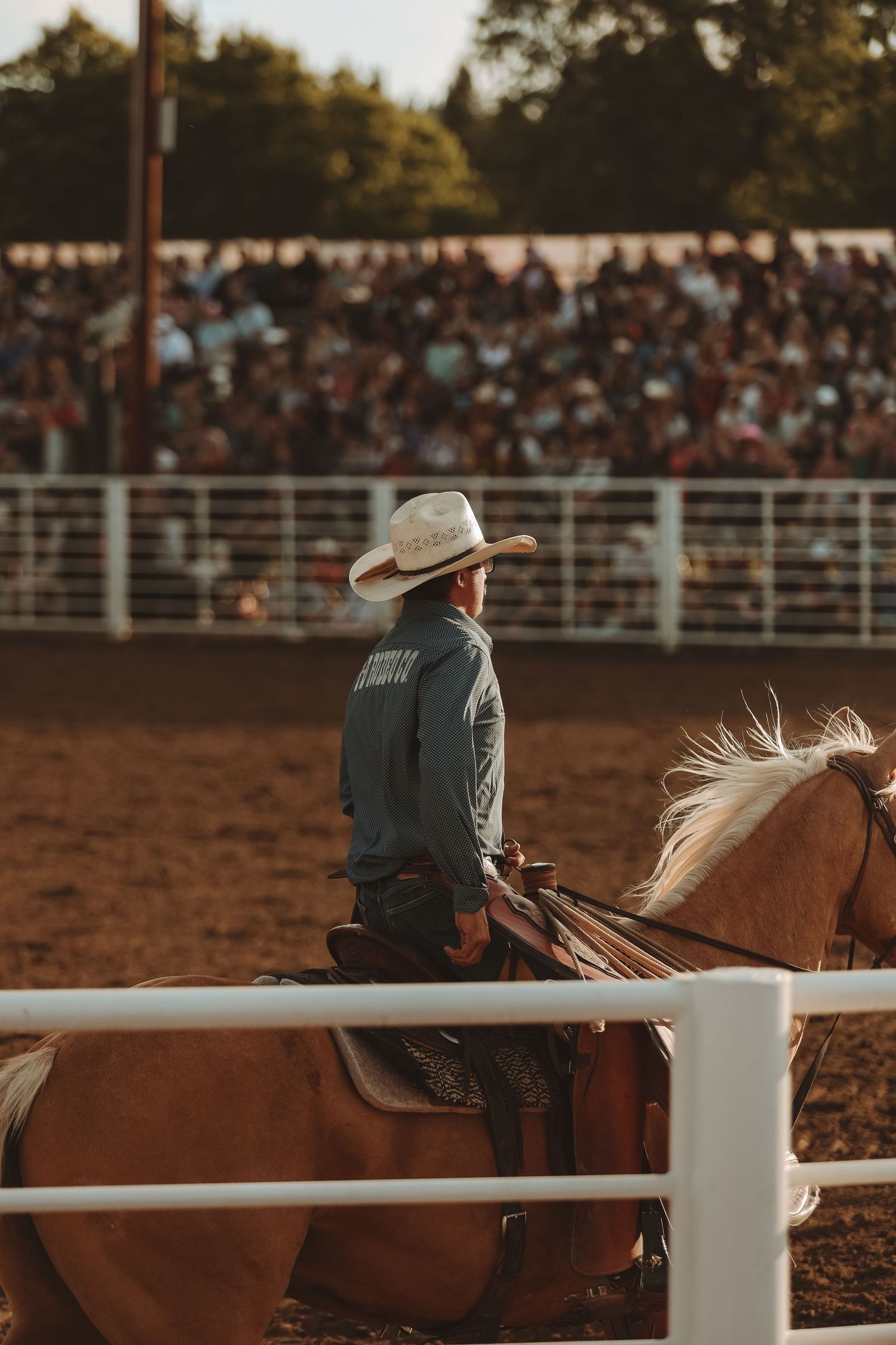Riders resting along the white arena fence during a golden hour rodeo event.