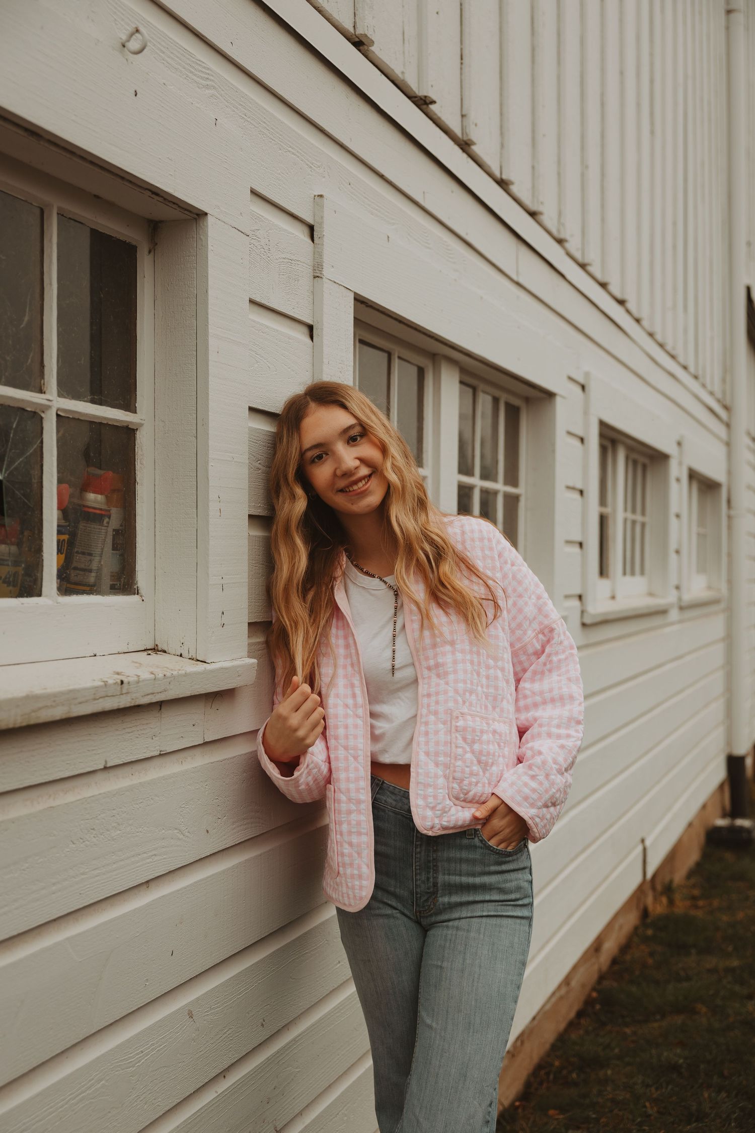 Fashion portrait series against white building exterior showing pink sweater and denim outfit styling.