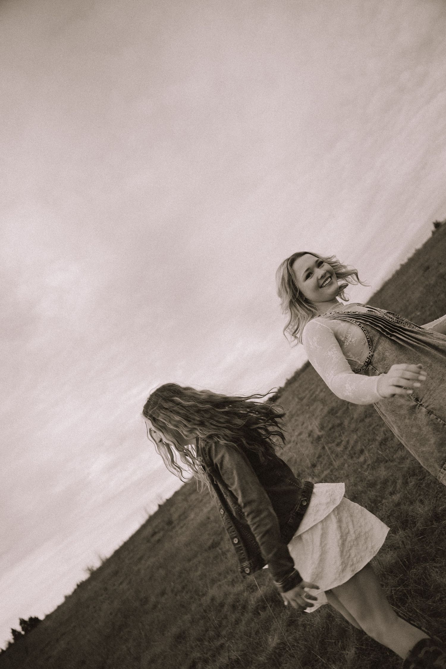 Two people dance and twirl joyfully in a field captured in dramatic black and white photography.