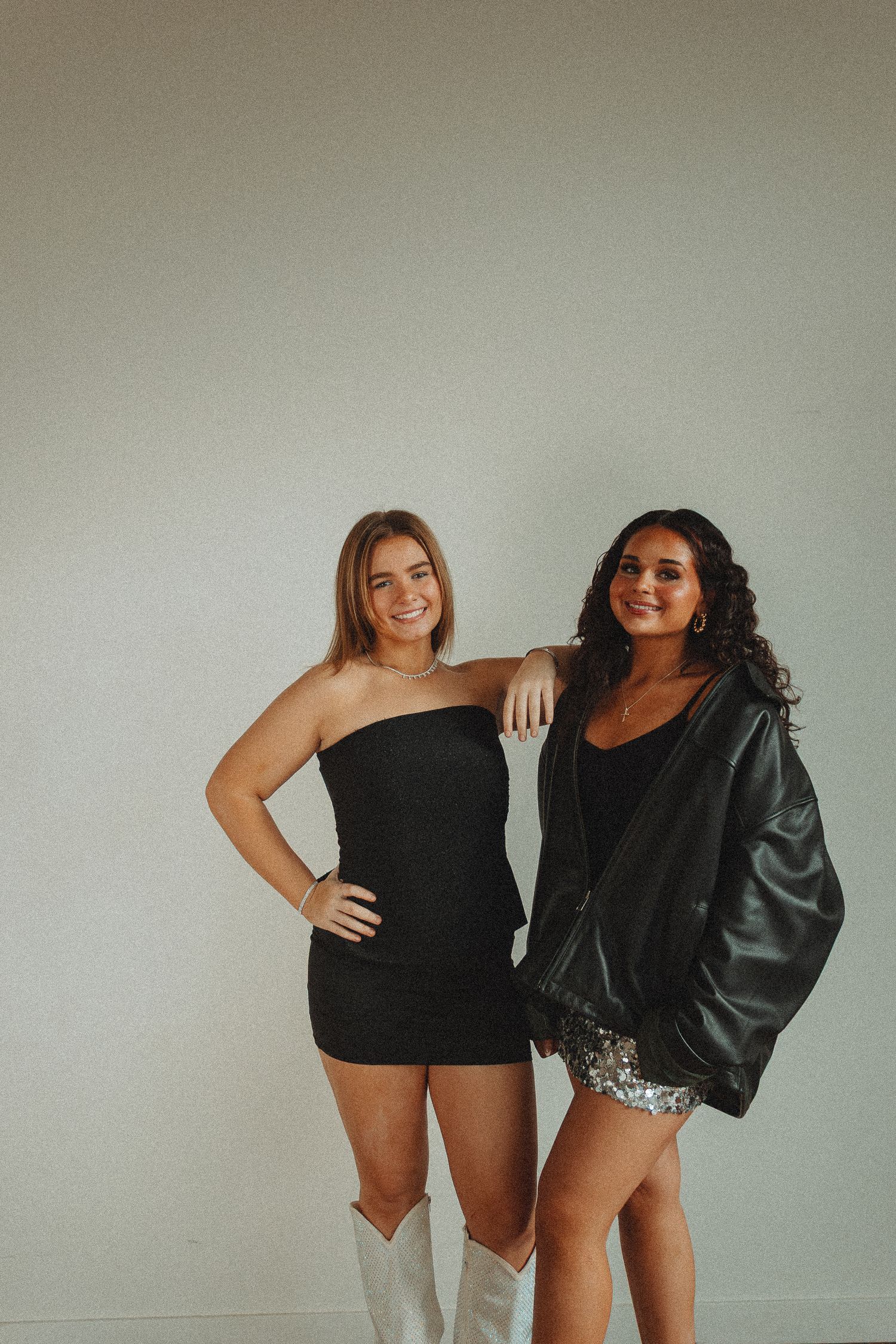 Two people posing together in black outfits and shorts against neutral background.