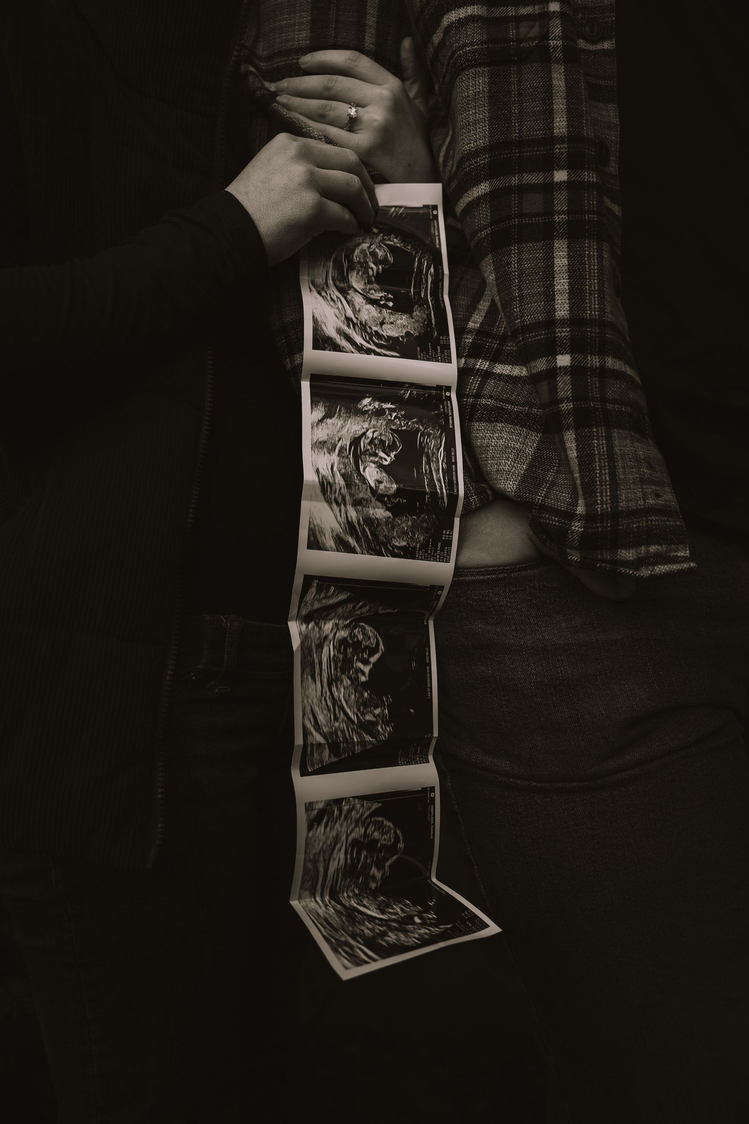 A sequence of black and white ultrasound photos being held and fanned out against a dark background.