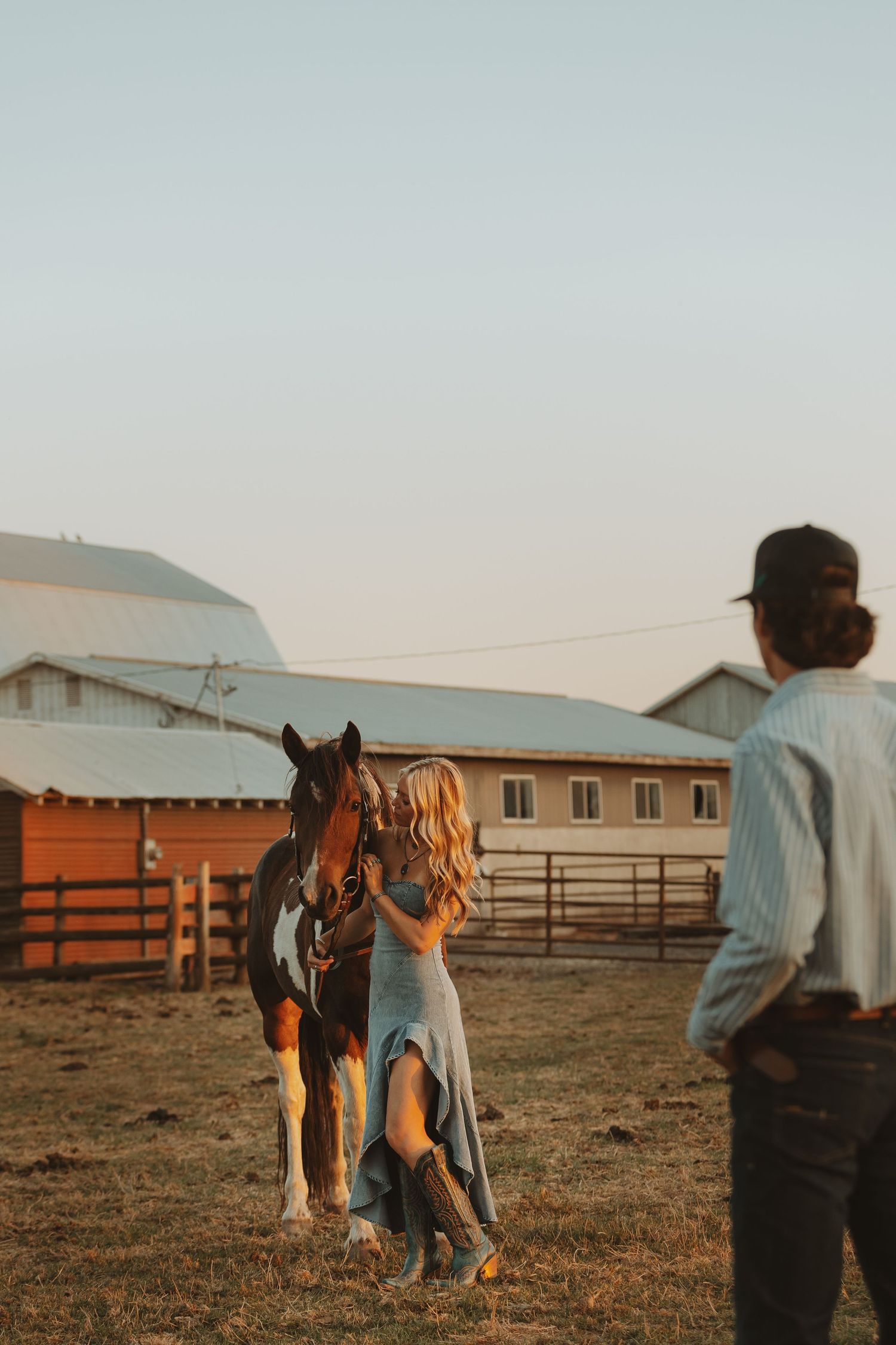A couple walks with their horse across a rural farm setting at dusk.