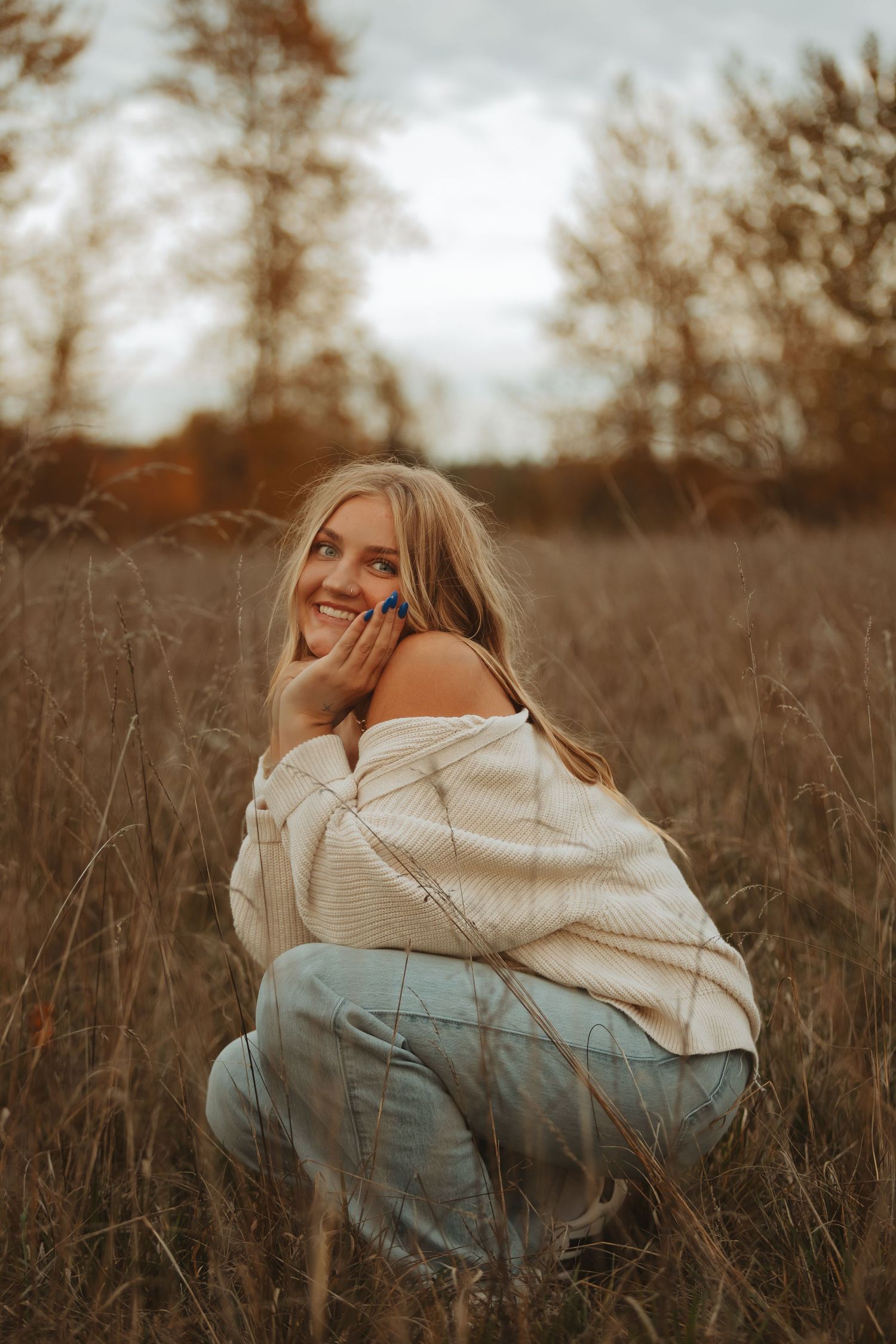 Person in cream sweater lies in autumn field during golden hour.