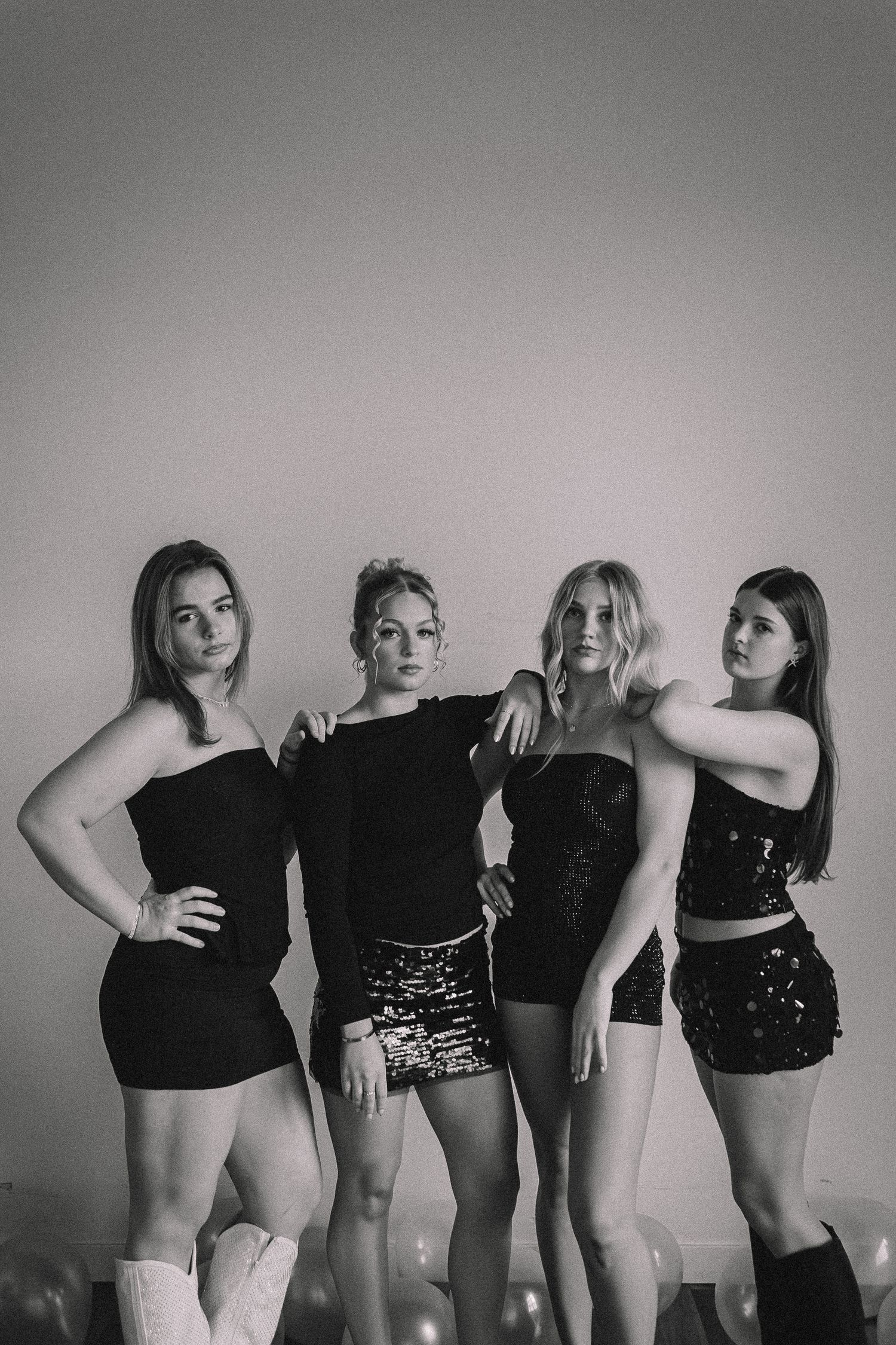 Black and white photo series showing four figures in black outfits posing together against a light background.