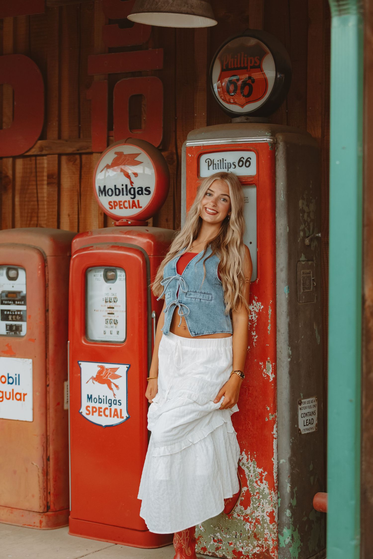 Classic gas station scene with vintage Phillips 66 and Mobilgas pumps against weathered red walls.