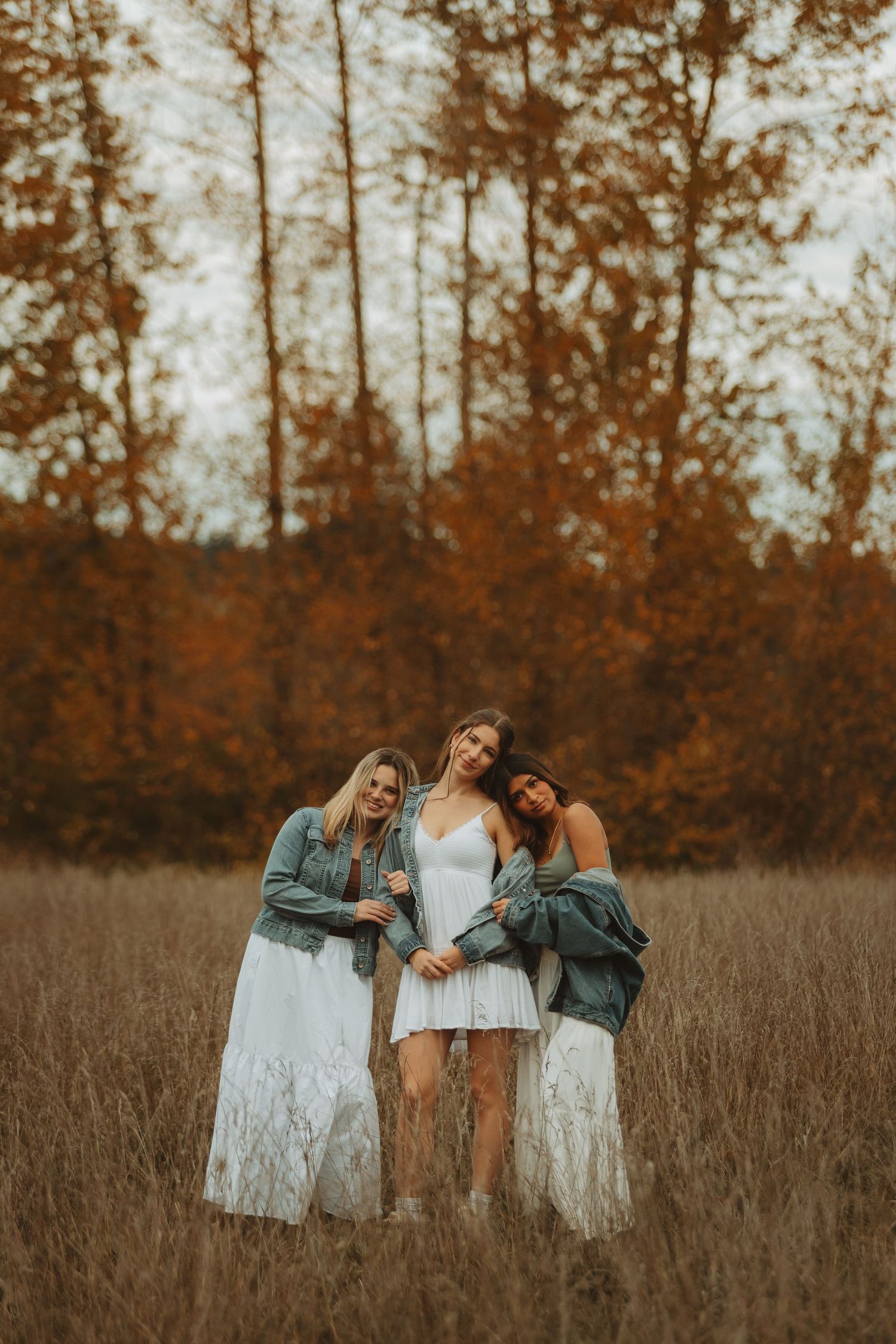 Group of friends embrace in a fall field with orange trees behind them at sunset.