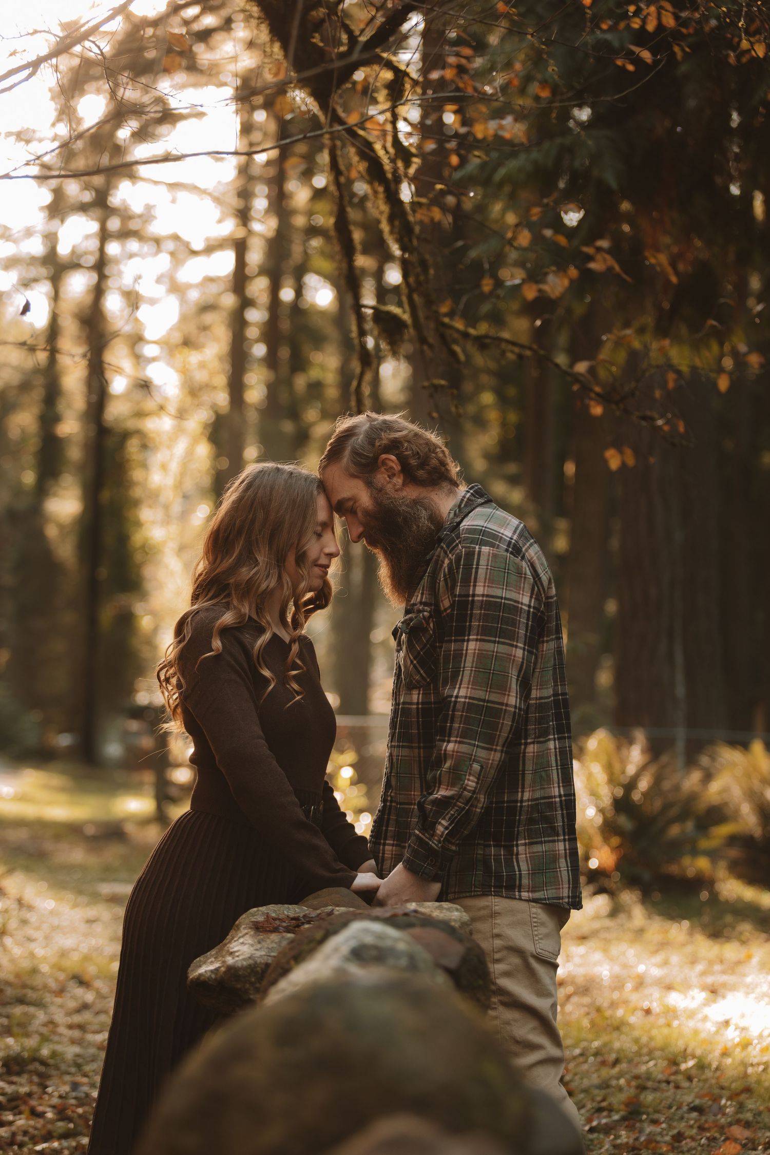 A romantic couple shares tender moments in a sunlit autumn forest setting with golden leaves and warm lighting.