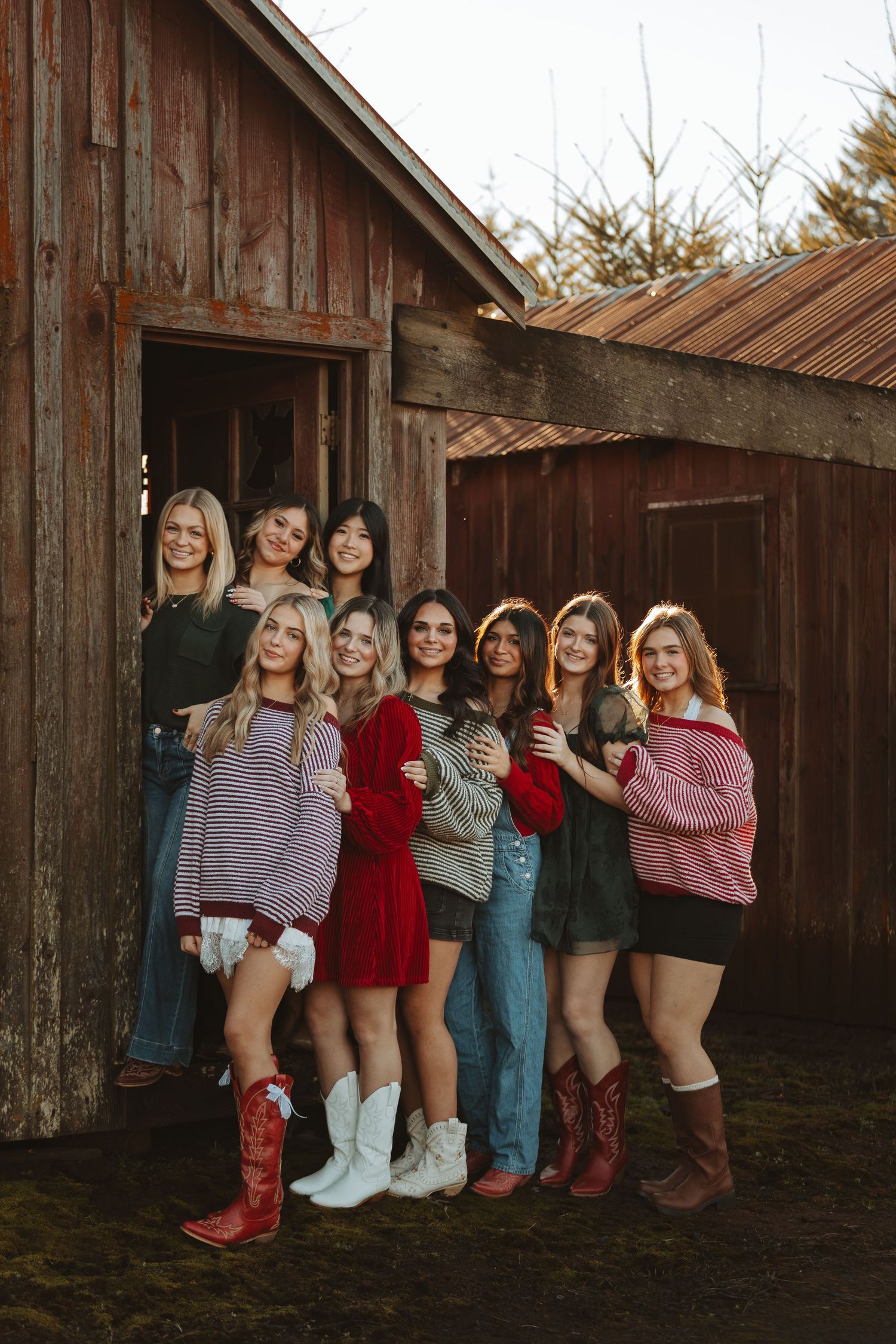 Group poses in casual fall outfits and boots outside rustic wooden barn in warm sunset lighting.
