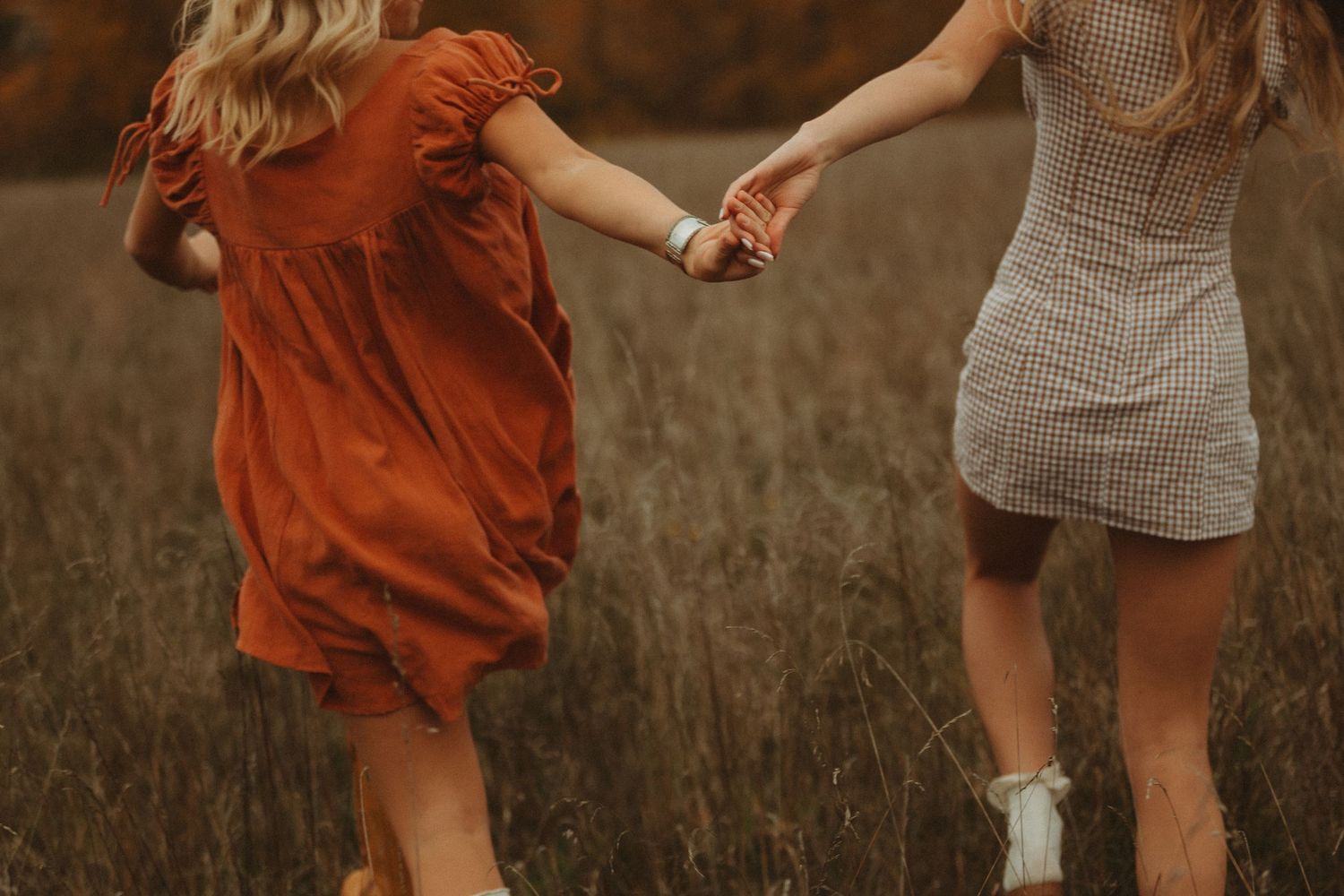 People dancing playfully in a field during sunset wearing orange and plaid dresses.