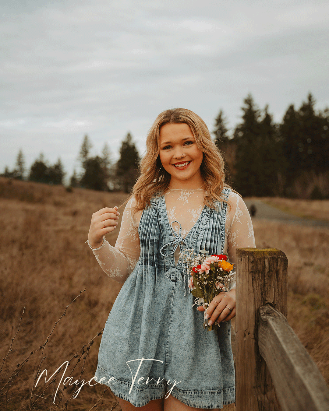 A woman in a denim top poses outdoors in a field during golden hour with colorful wildflowers.