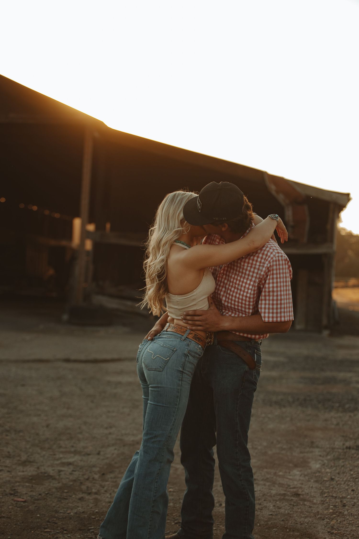 Couple embraces warmly at sunset outside a weathered barn.