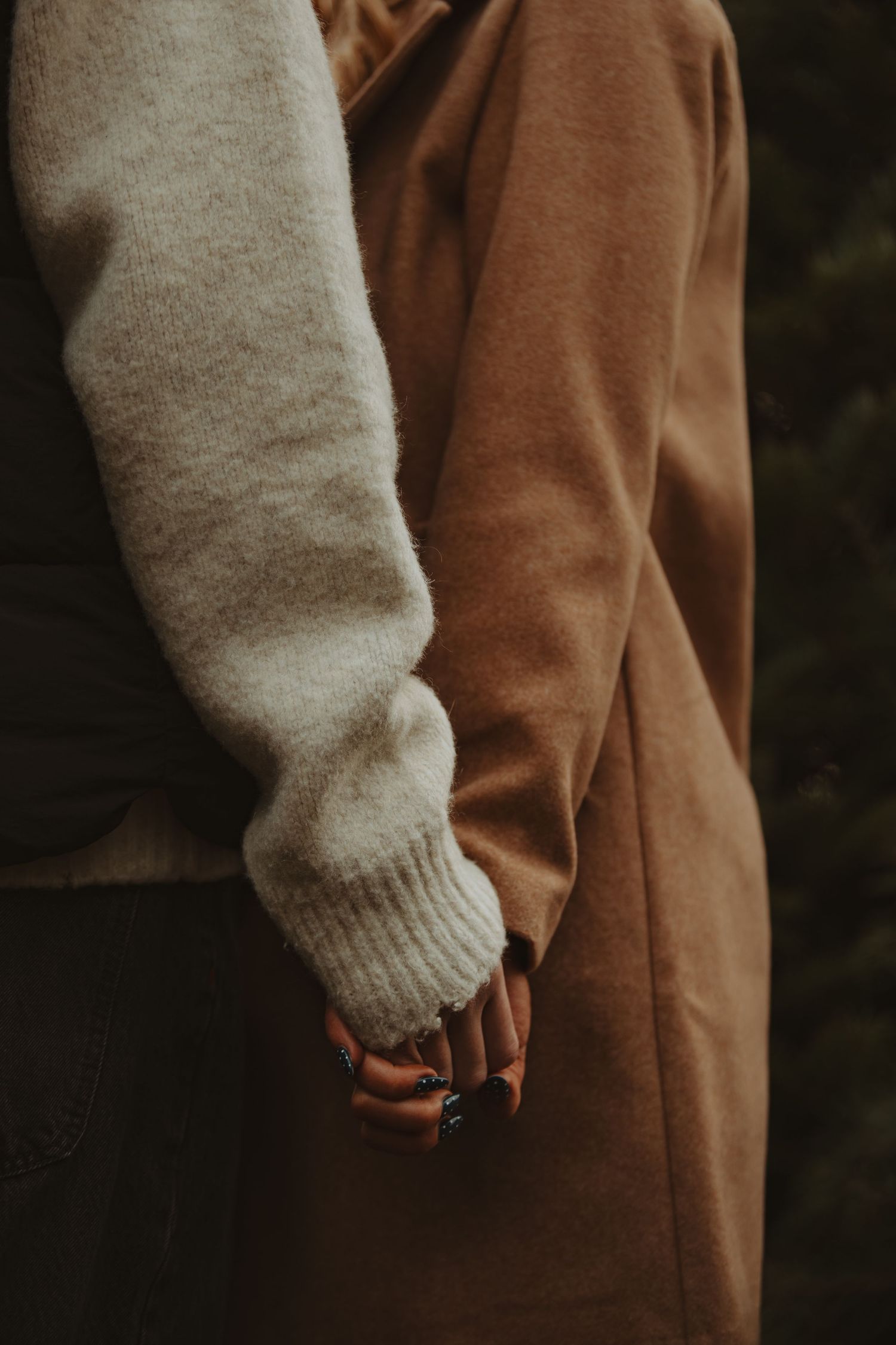 Close-up shot of two people holding hands, one wearing a beige sweater and the other in a brown coat.