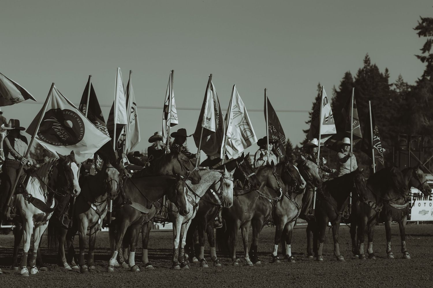 A line of riders on horseback hold flags during a ceremonial display at a rodeo event.
