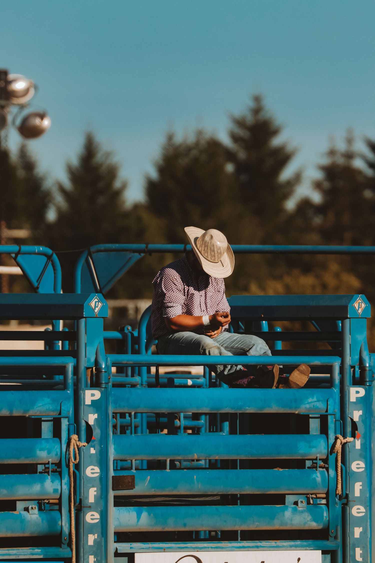 Spectators watch from blue bleachers at an outdoor rodeo event during daytime.