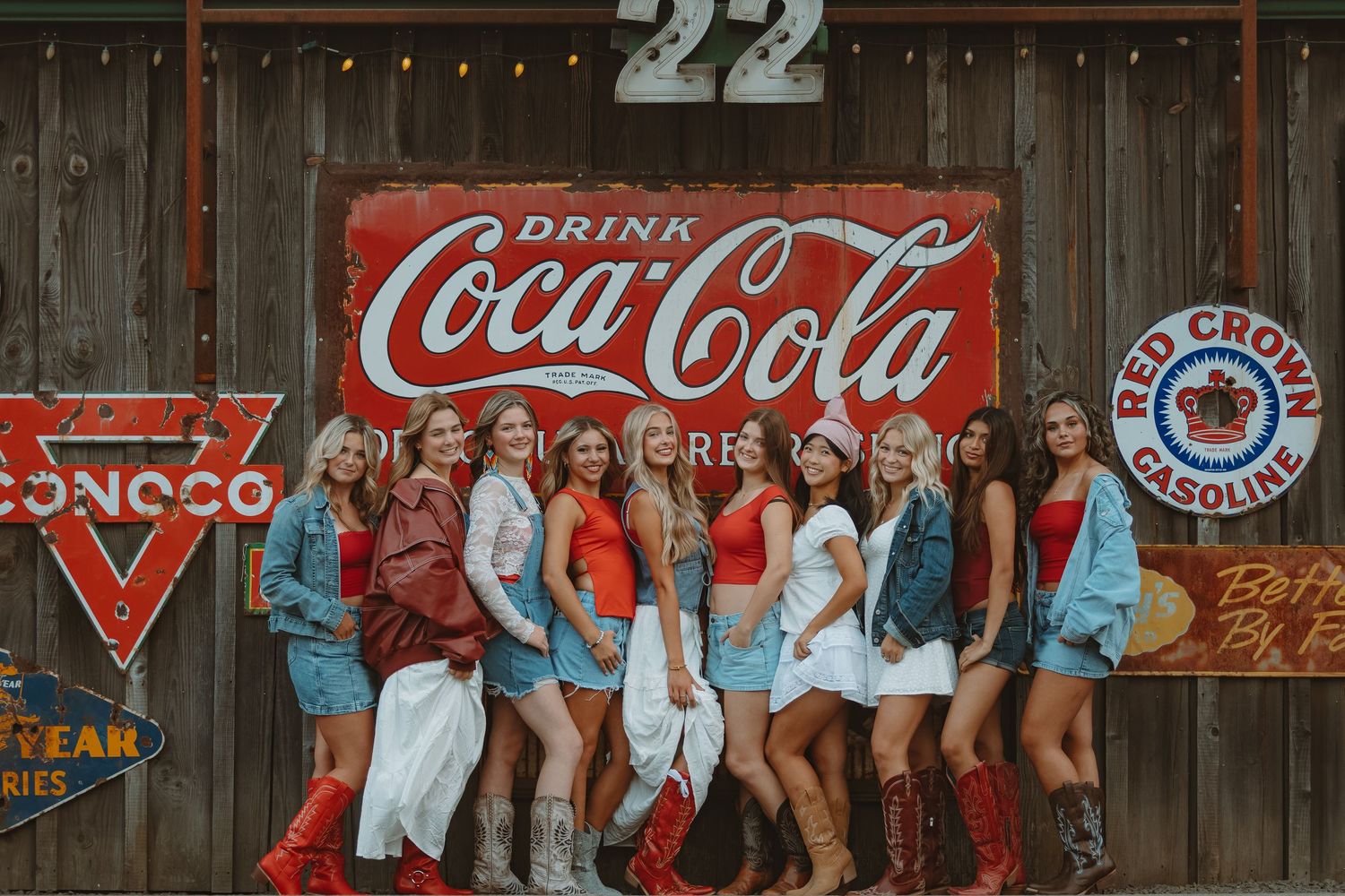 A rustic wooden wall decorated with vintage Coca-Cola signs and string lights creating a retro atmosphere.
