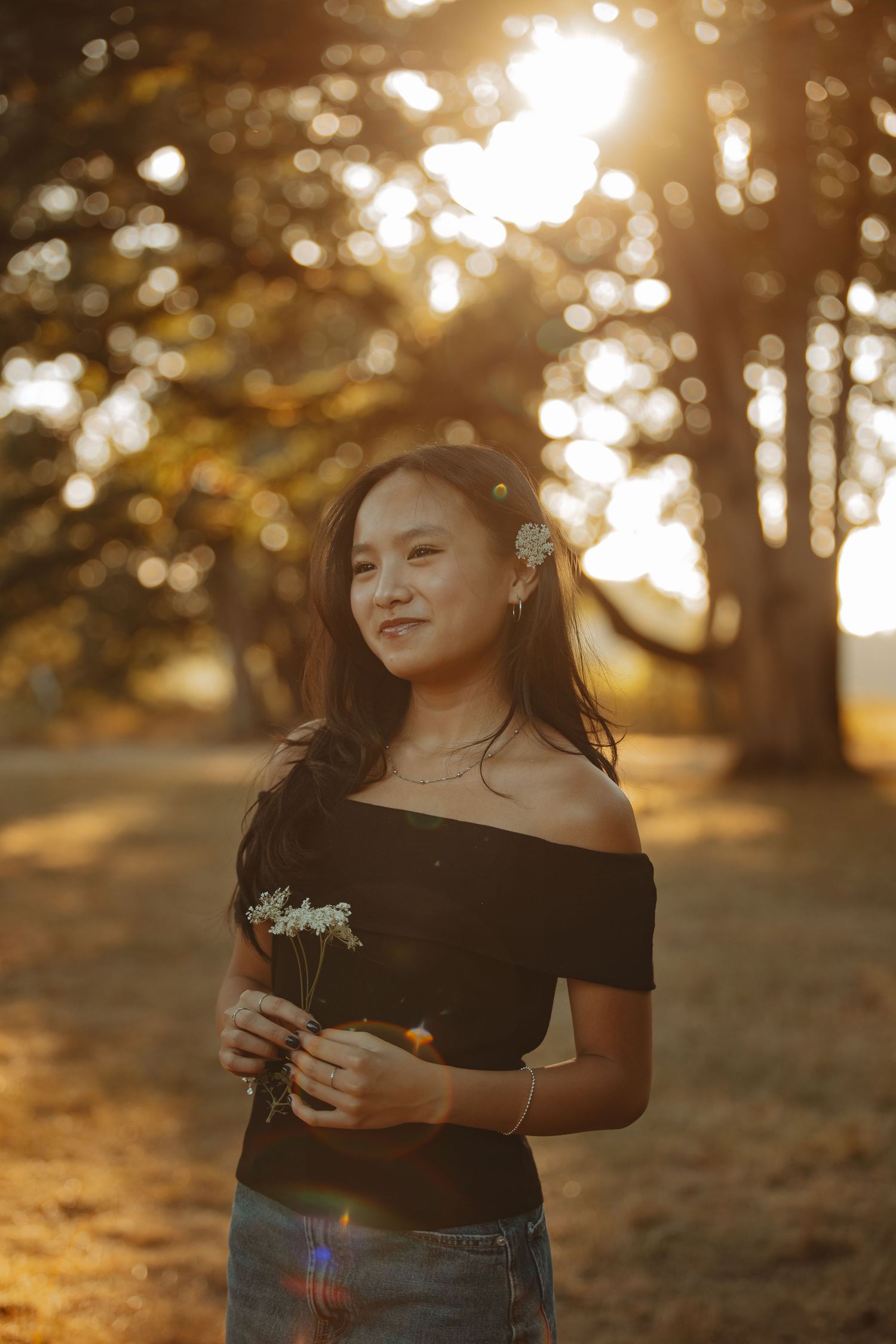 A person in a black top poses outdoors during golden hour sunlight creating a warm, dreamy atmosphere.