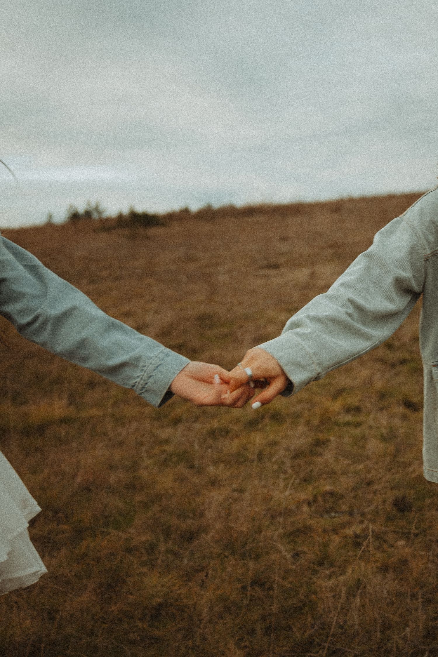 Two people reaching out to hold hands in a tender moment against a moody autumn landscape.