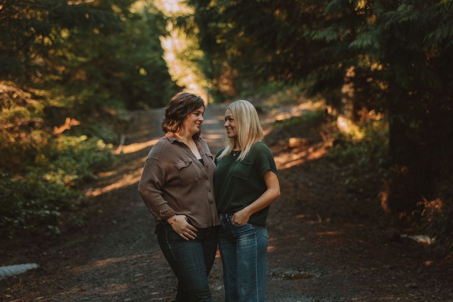 A couple embraces and laughs together on a forest path in warm evening light.