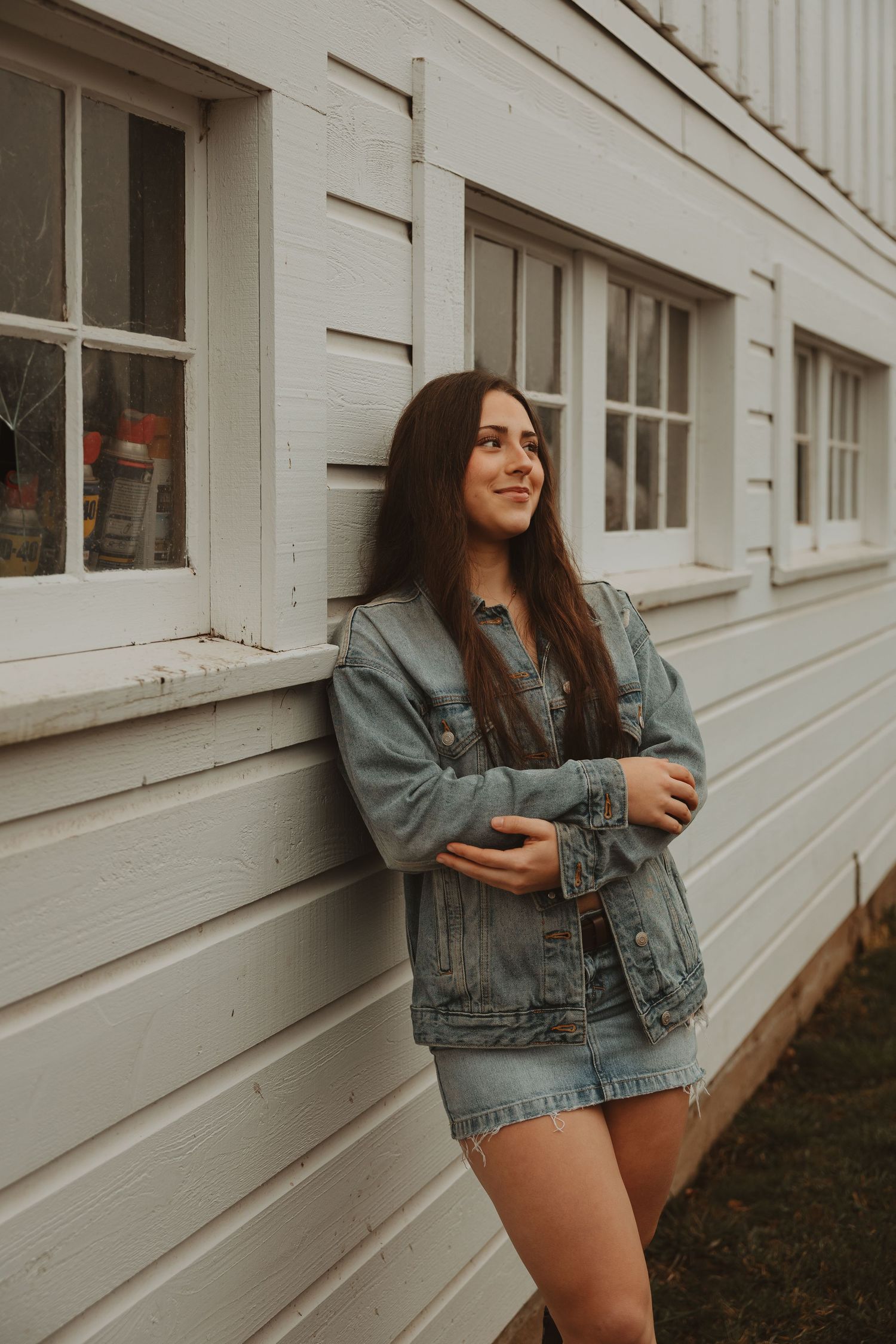 Casual outdoor portrait session with denim jacket against white siding wall.