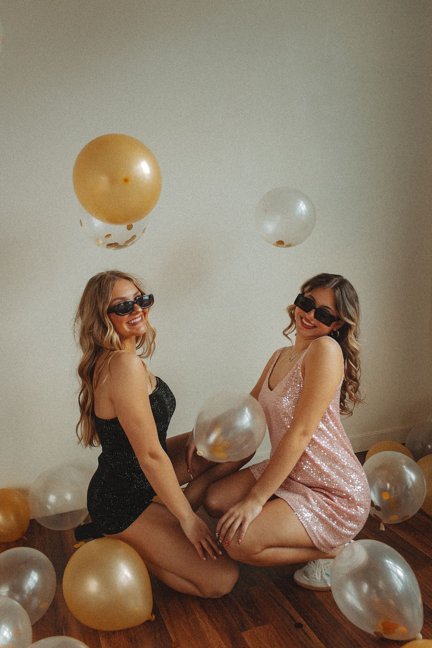 Two people in black and sparkly outfits pose with gold and silver balloons.