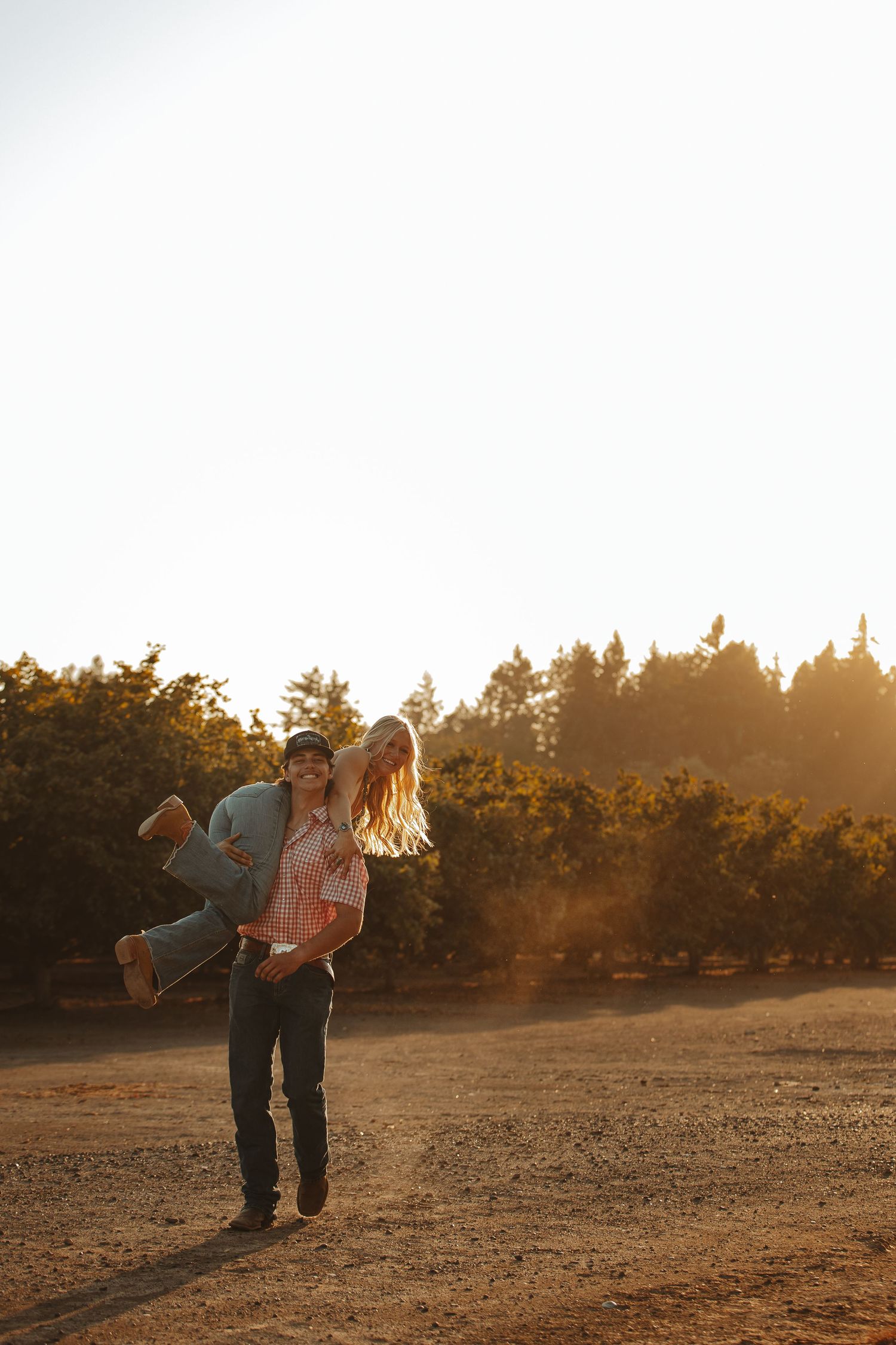 Couple playfully dancing in an orchard at sunset.