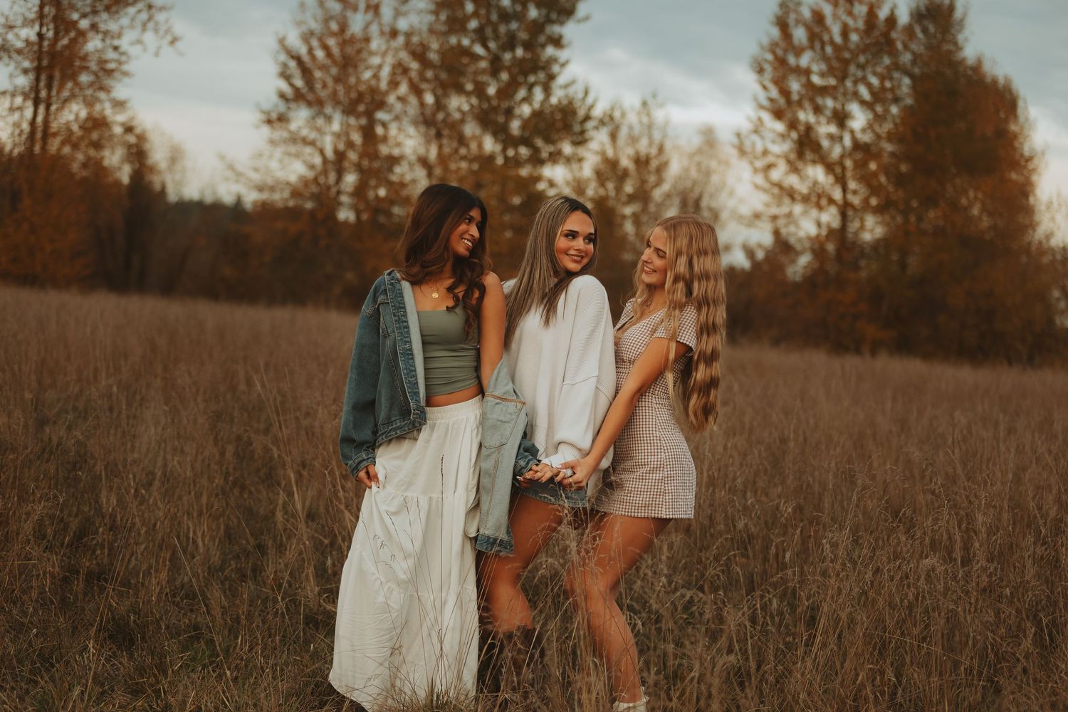 Two people walking through autumn field at sunset wearing casual dresses.
