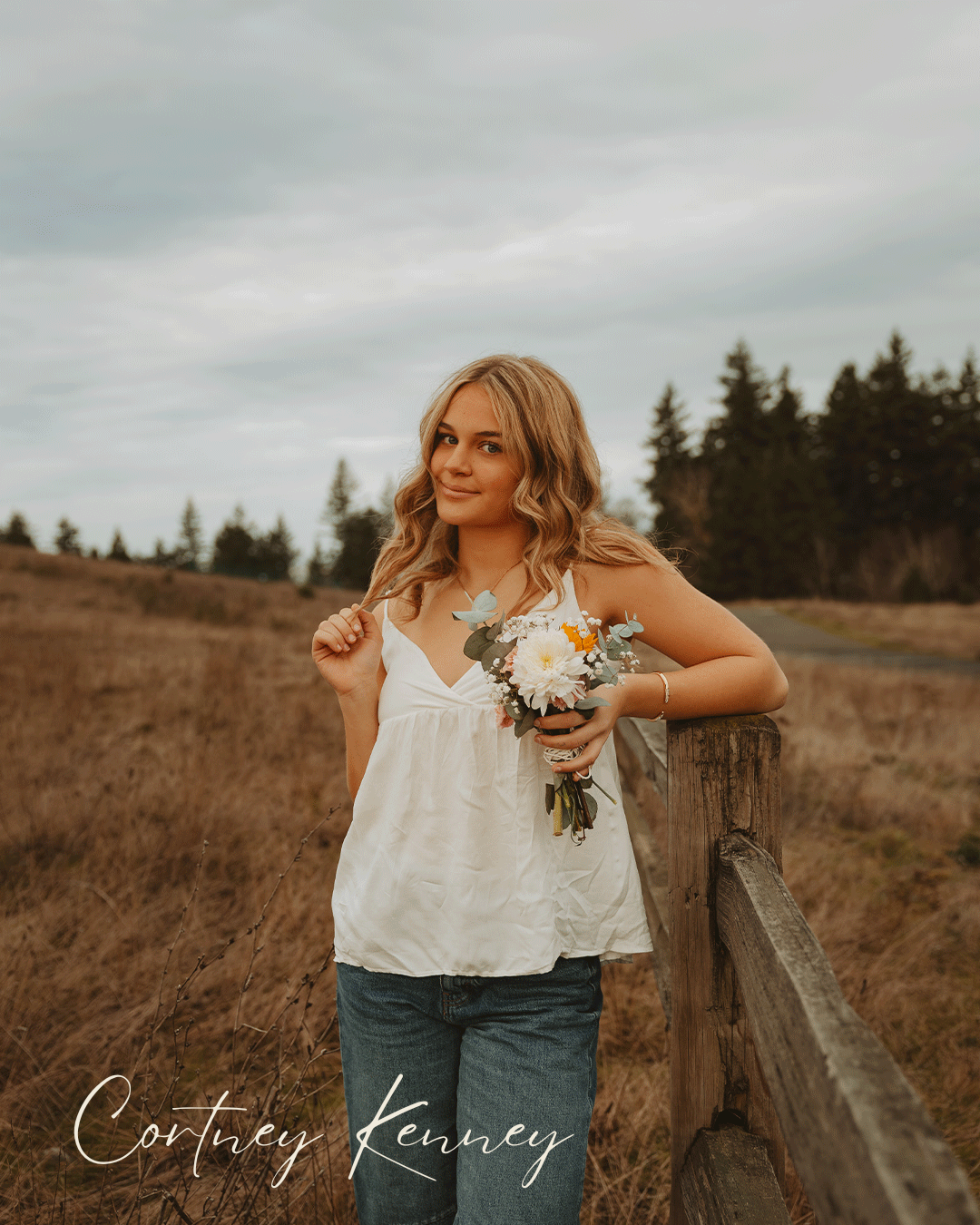 A rustic outdoor scene with someone in jeans and a white top leaning against a wooden fence at golden hour.