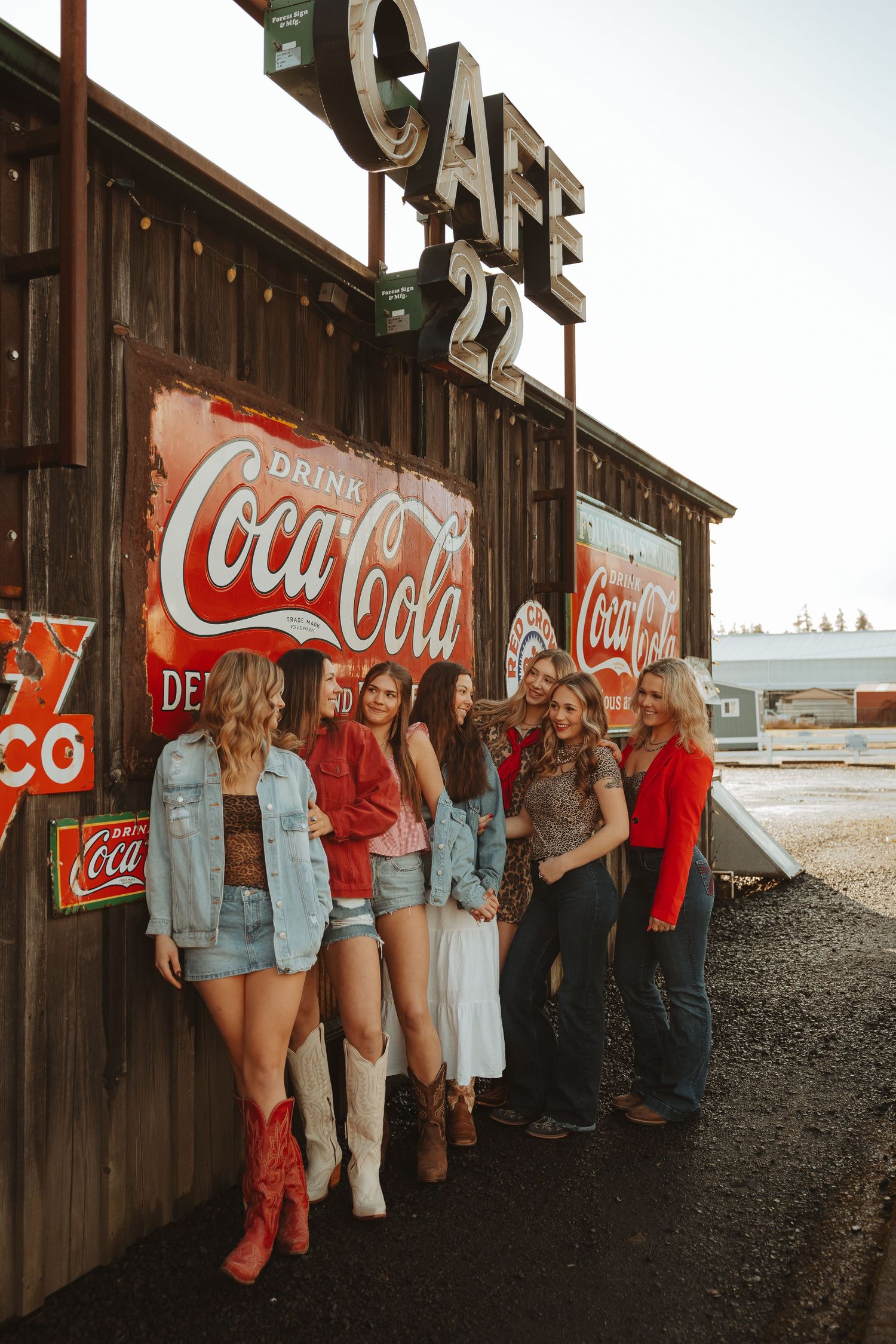 Group of women in western outfits posing outside rustic Cafe 22 with vintage Coca-Cola signs.