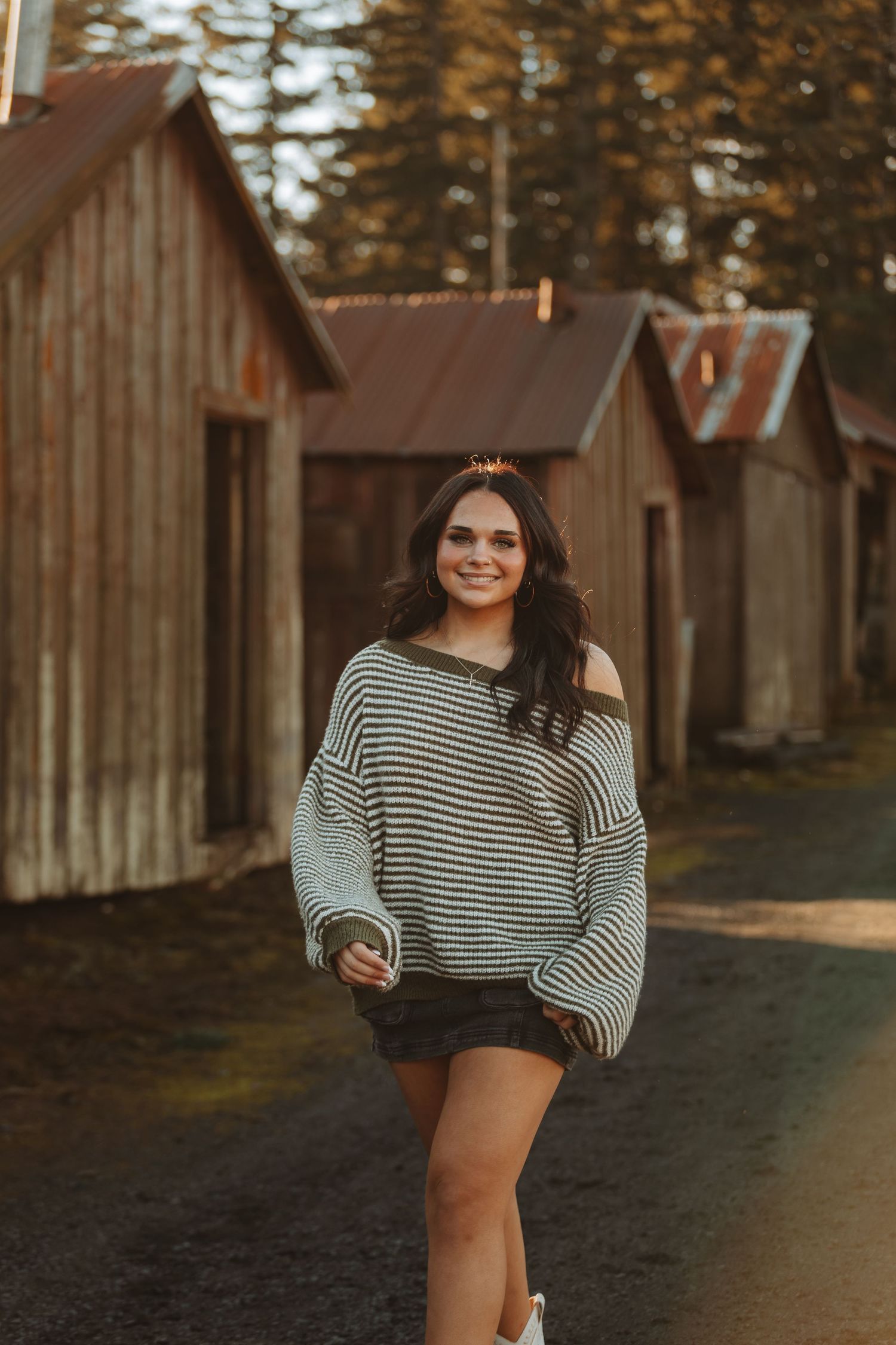 Person in striped top poses playfully near wooden cabins during golden hour.