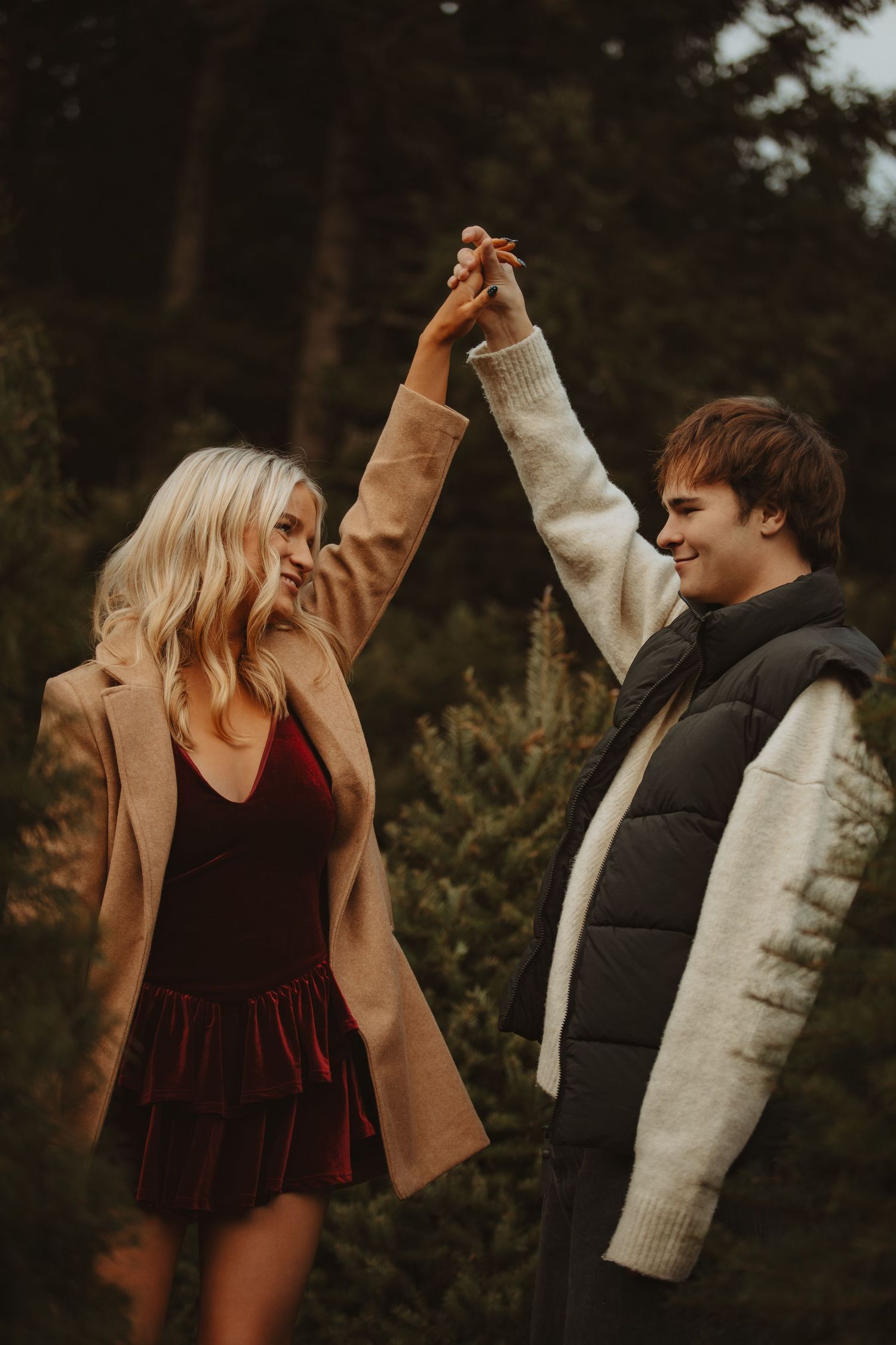 Joyful couple dancing and holding hands high among pine trees in autumn attire.