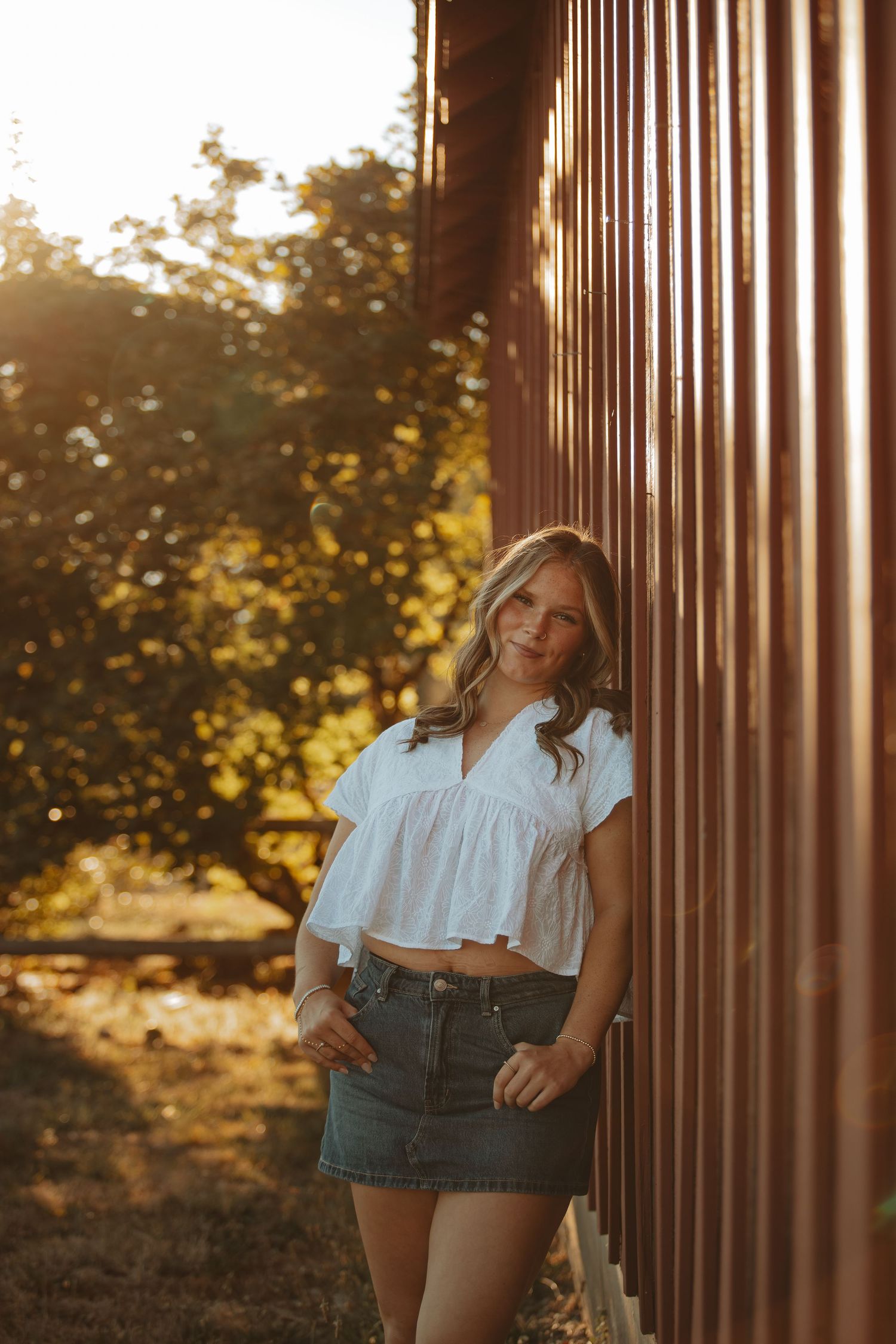 Summer portrait session against wooden pillars in warm evening light.