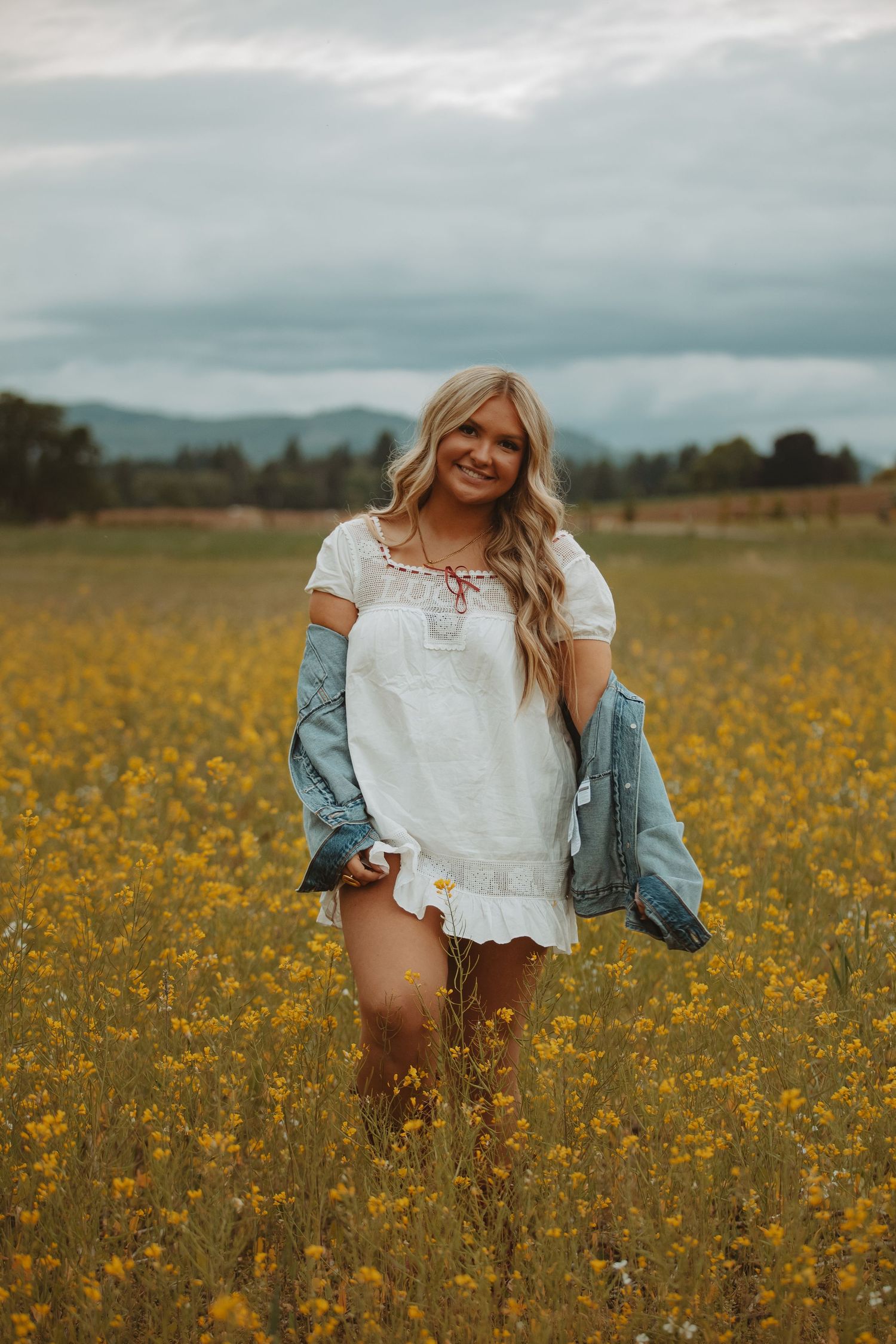 Person in white top and denim jacket dancing through a field of yellow flowers.