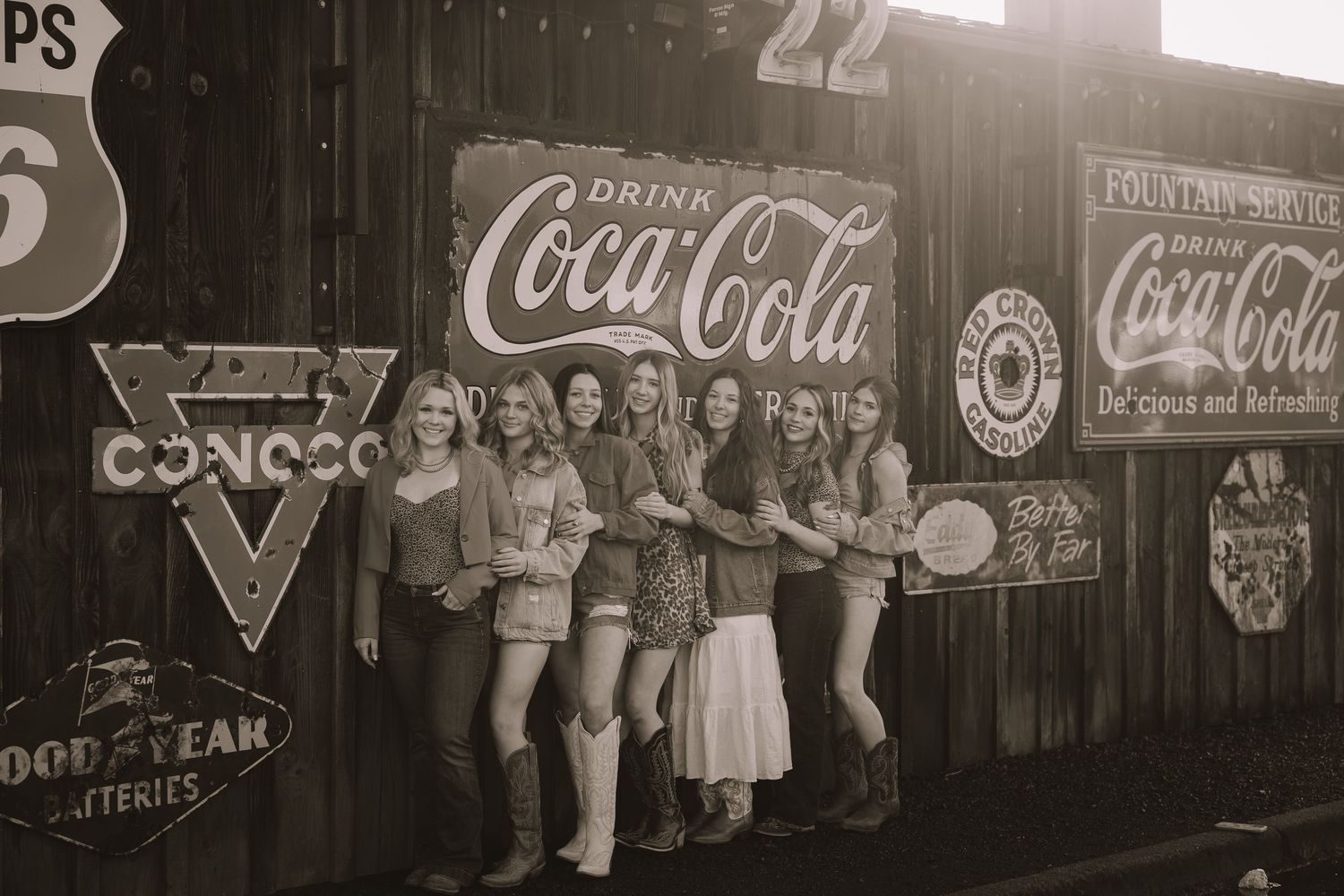 Group of women posing in front of vintage Coca-Cola signs and retro advertisements in a sepia-toned photo.