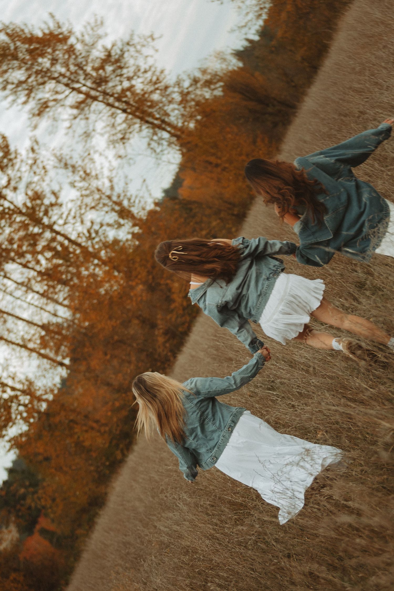 A figure in a denim jacket and white dress dances gracefully in a golden autumn field at sunset.