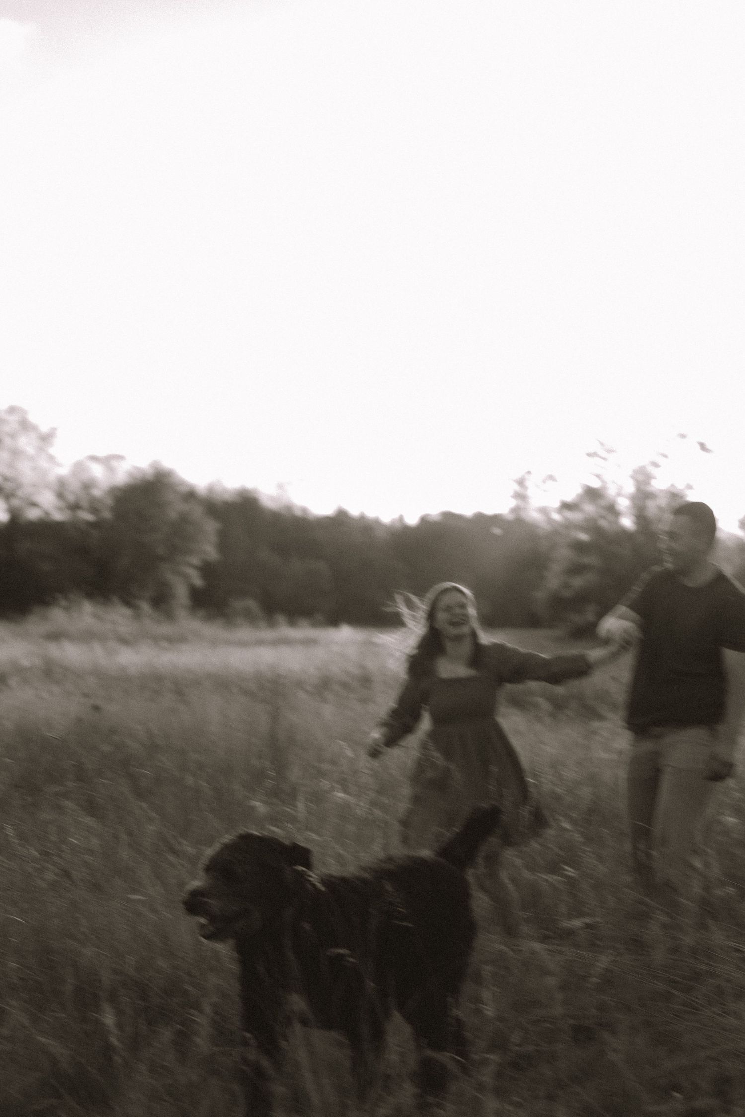 Black and white photo of people enjoying themselves in a tall grass field at dusk.