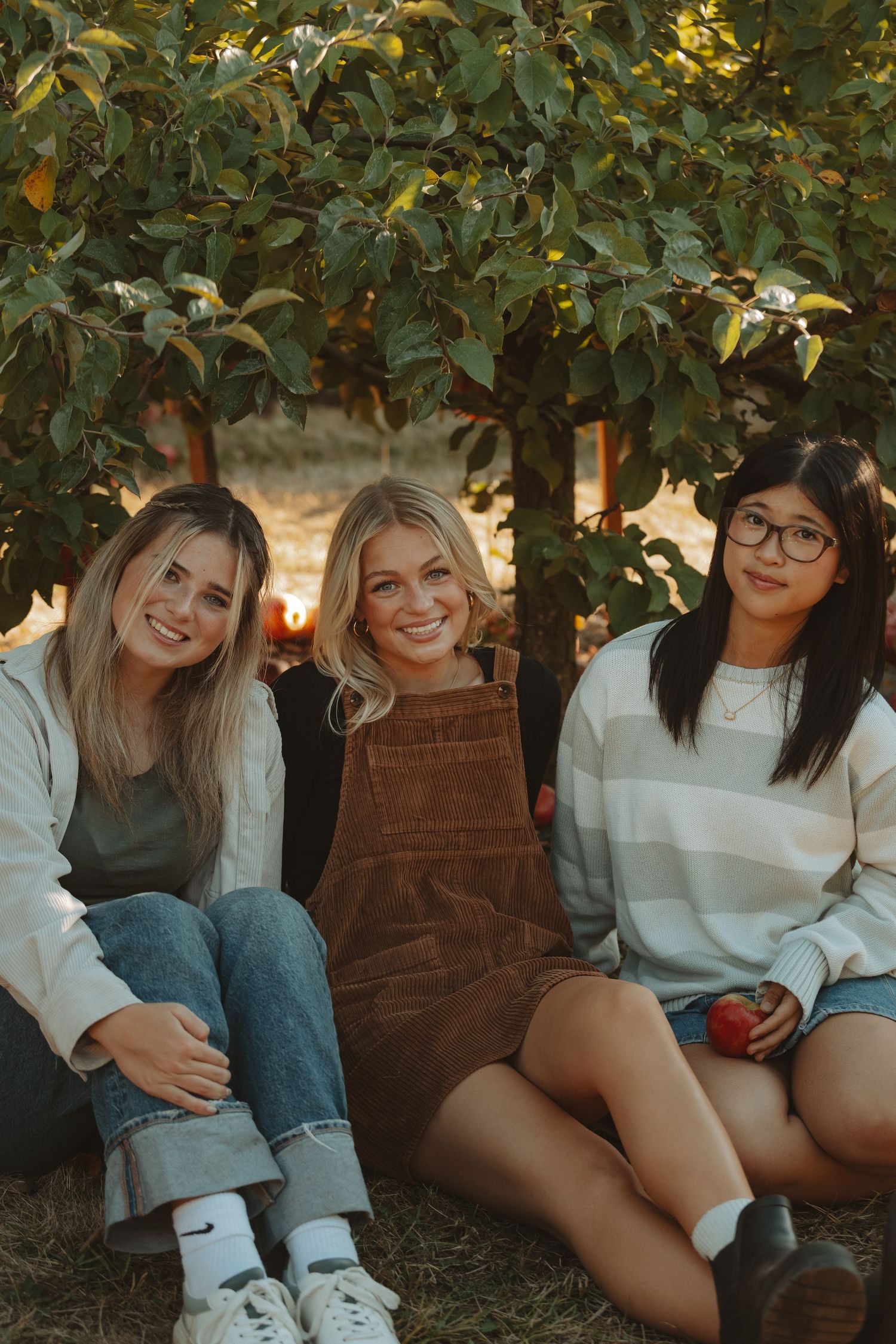 Group relaxing beneath fruit trees during golden hour wearing casual fall outfits.
