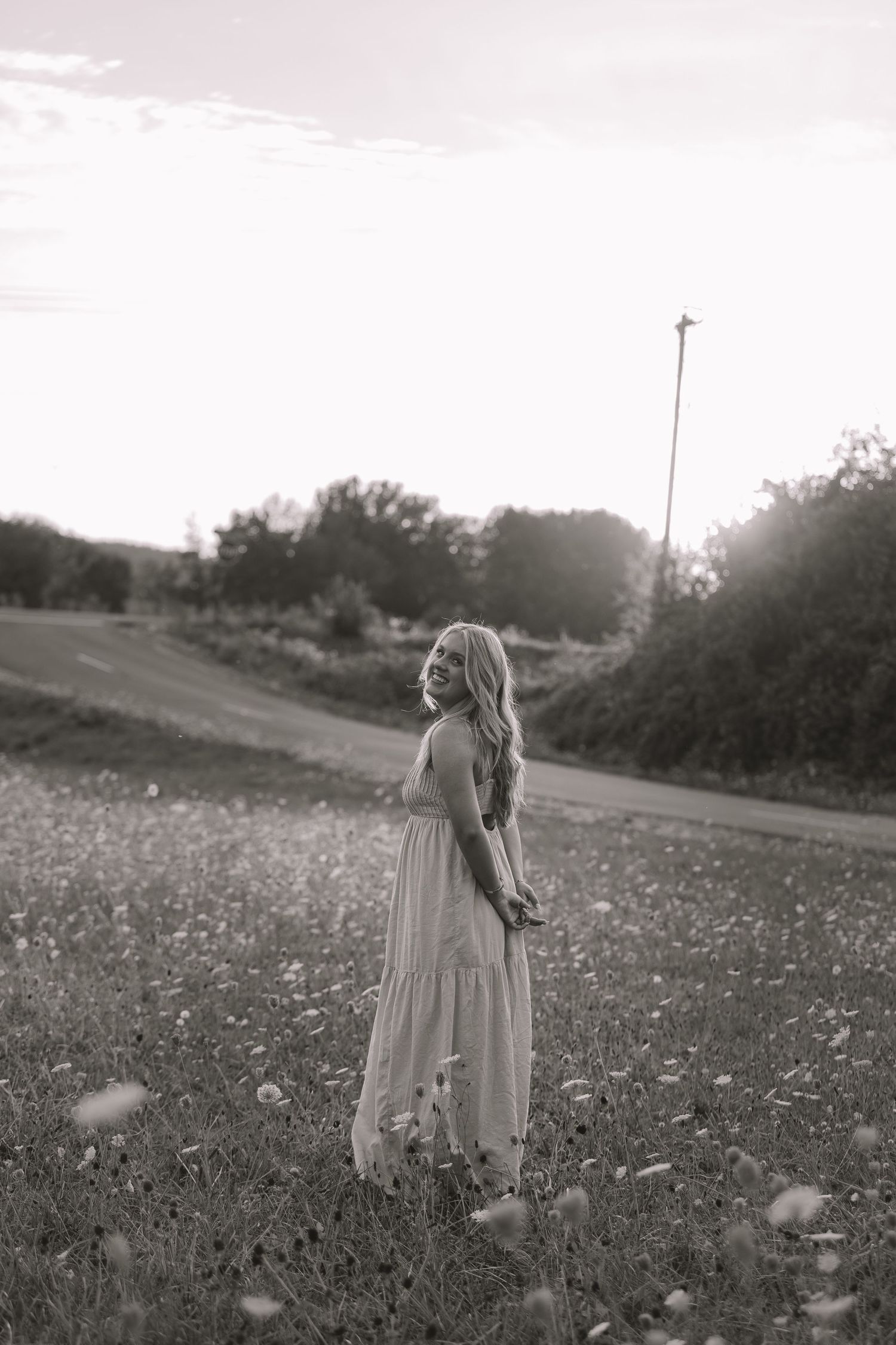 Black and white photo of a woman in a flowing dress standing in a wildflower field at sunset.