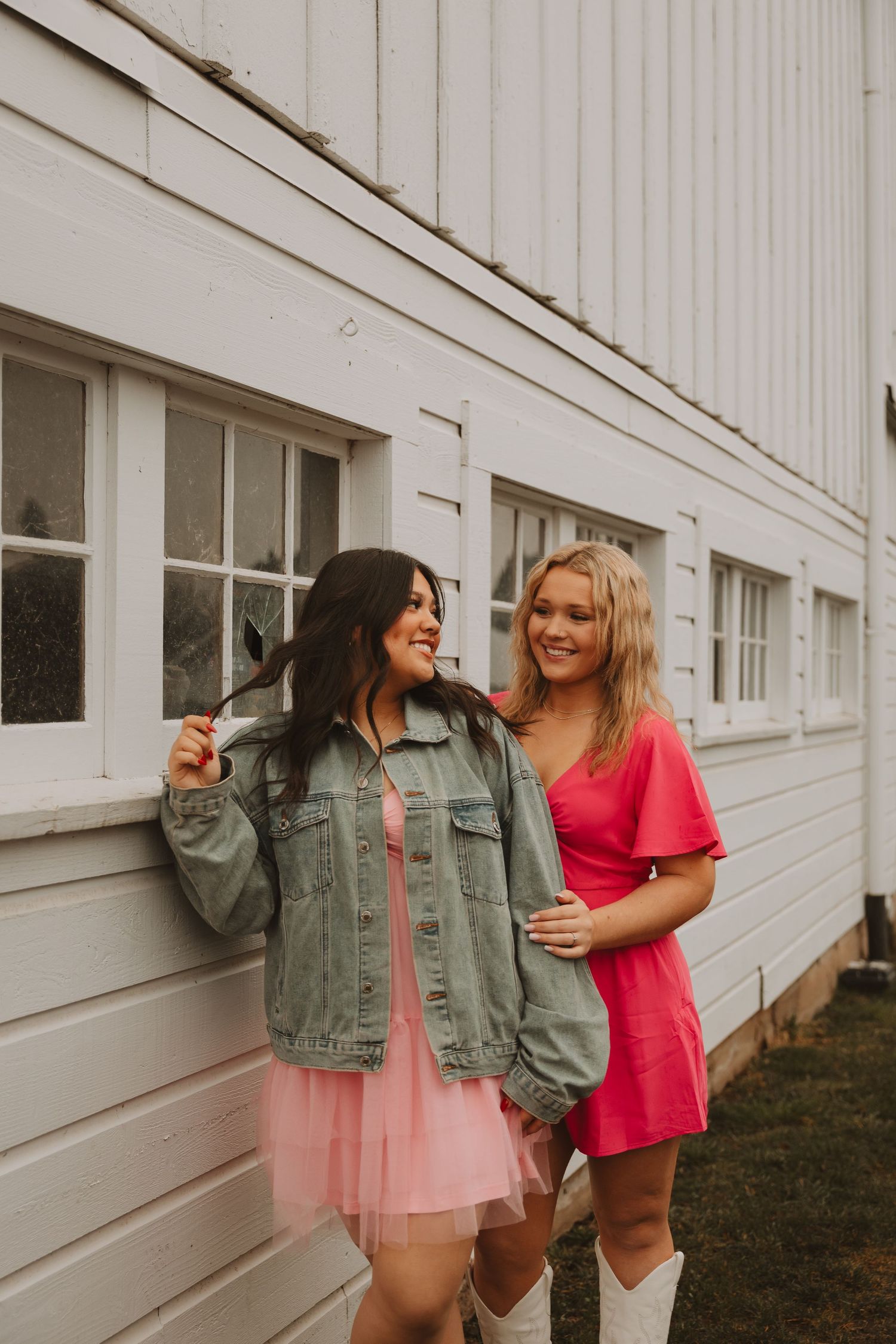 Friends in casual outfits posing playfully against white siding of building.