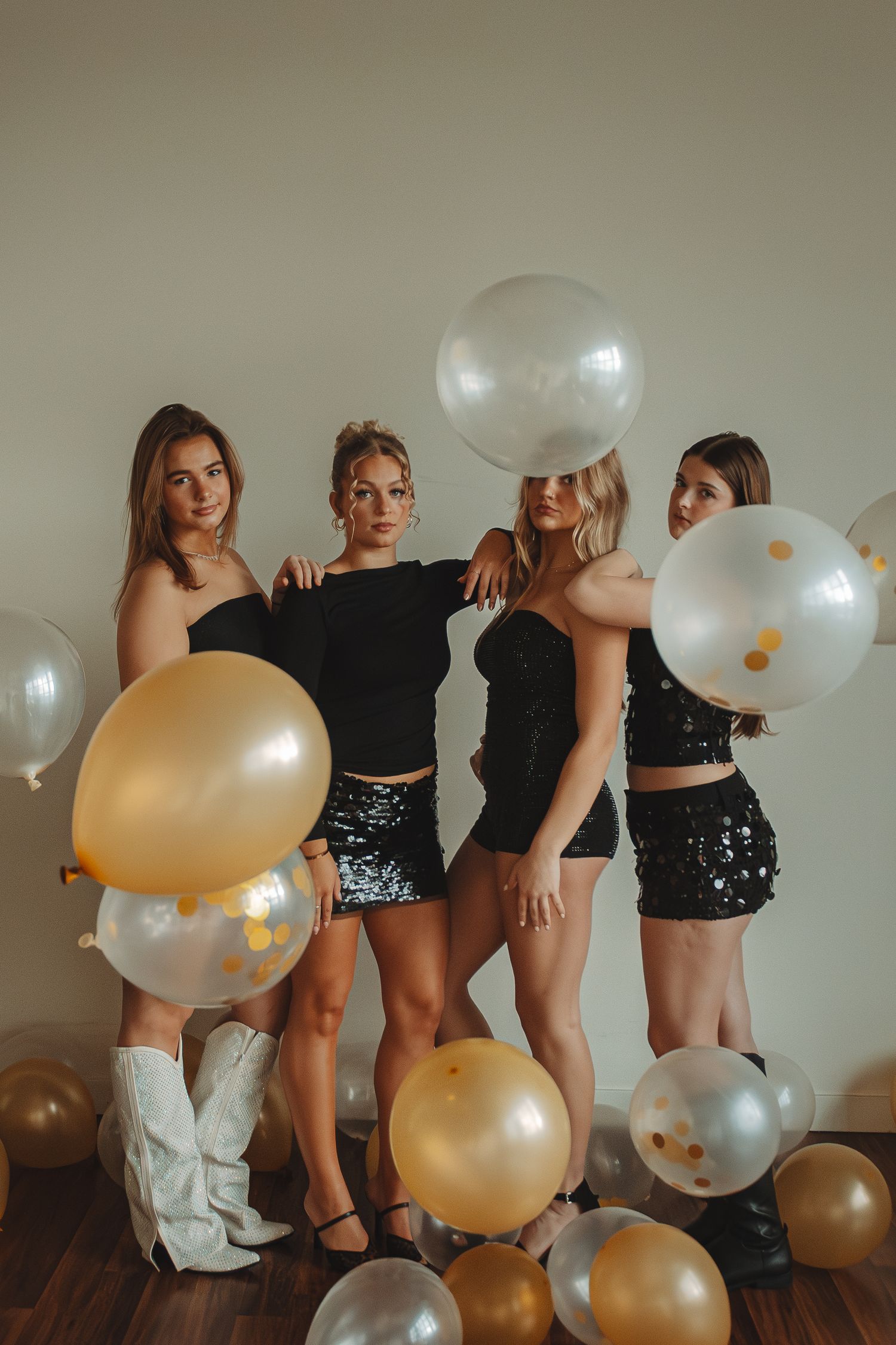 Group photoshoot with gold and white balloons on hardwood floor.