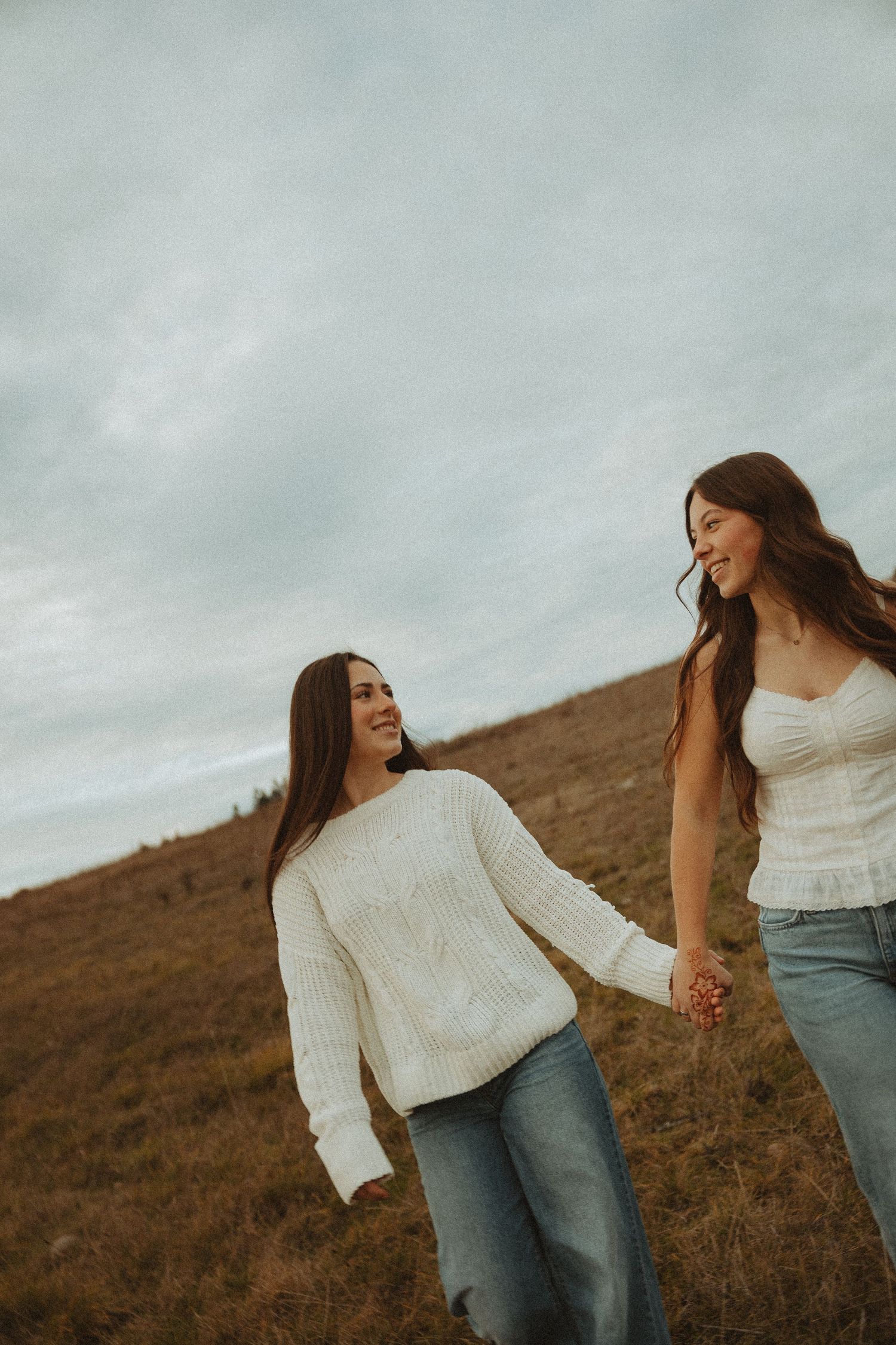 Two people in casual attire walking together on a hillside against an overcast sky.