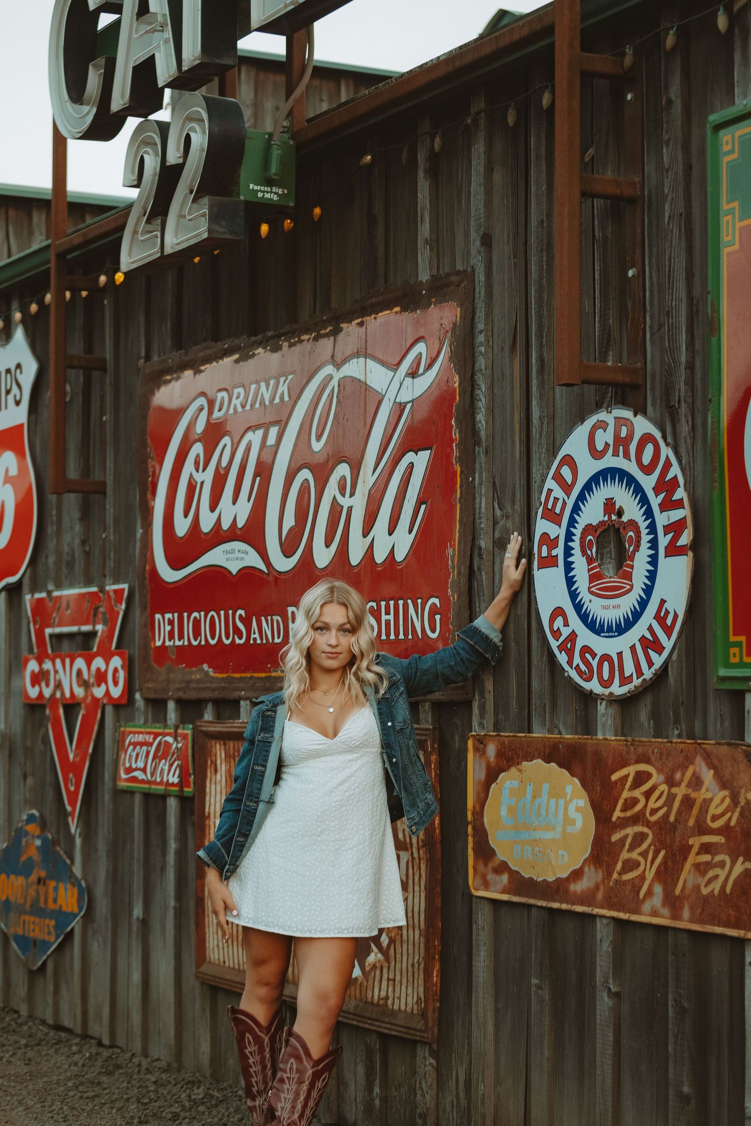 Vintage Coca-Cola signs and retro advertisements decorate a rustic wooden wall with string lights.