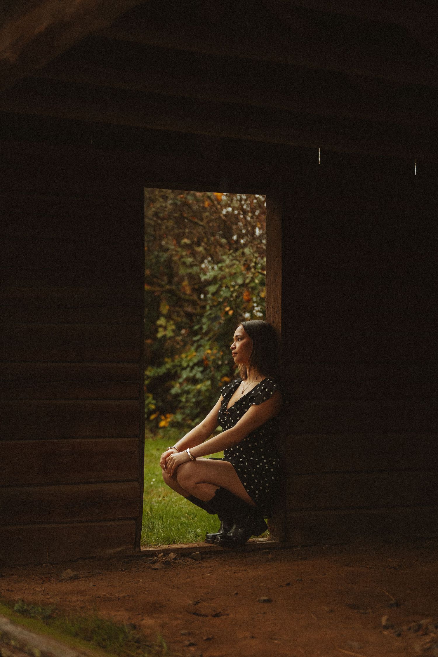 A silhouetted figure sits in a rustic wooden window frame as sunlight streams through from a garden setting.