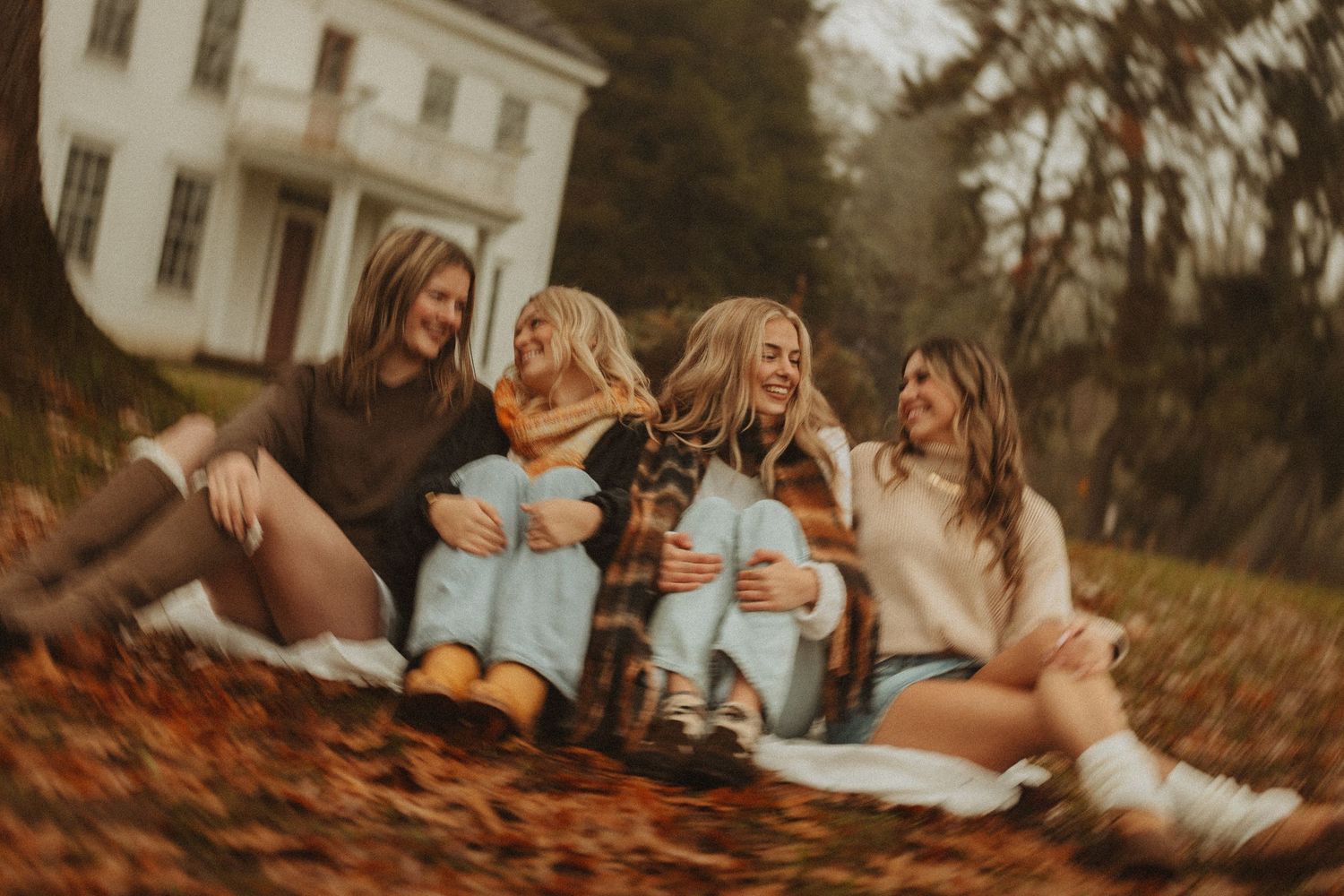 People in casual attire lying on fallen leaves displaying coordinated socks near a colonial house.