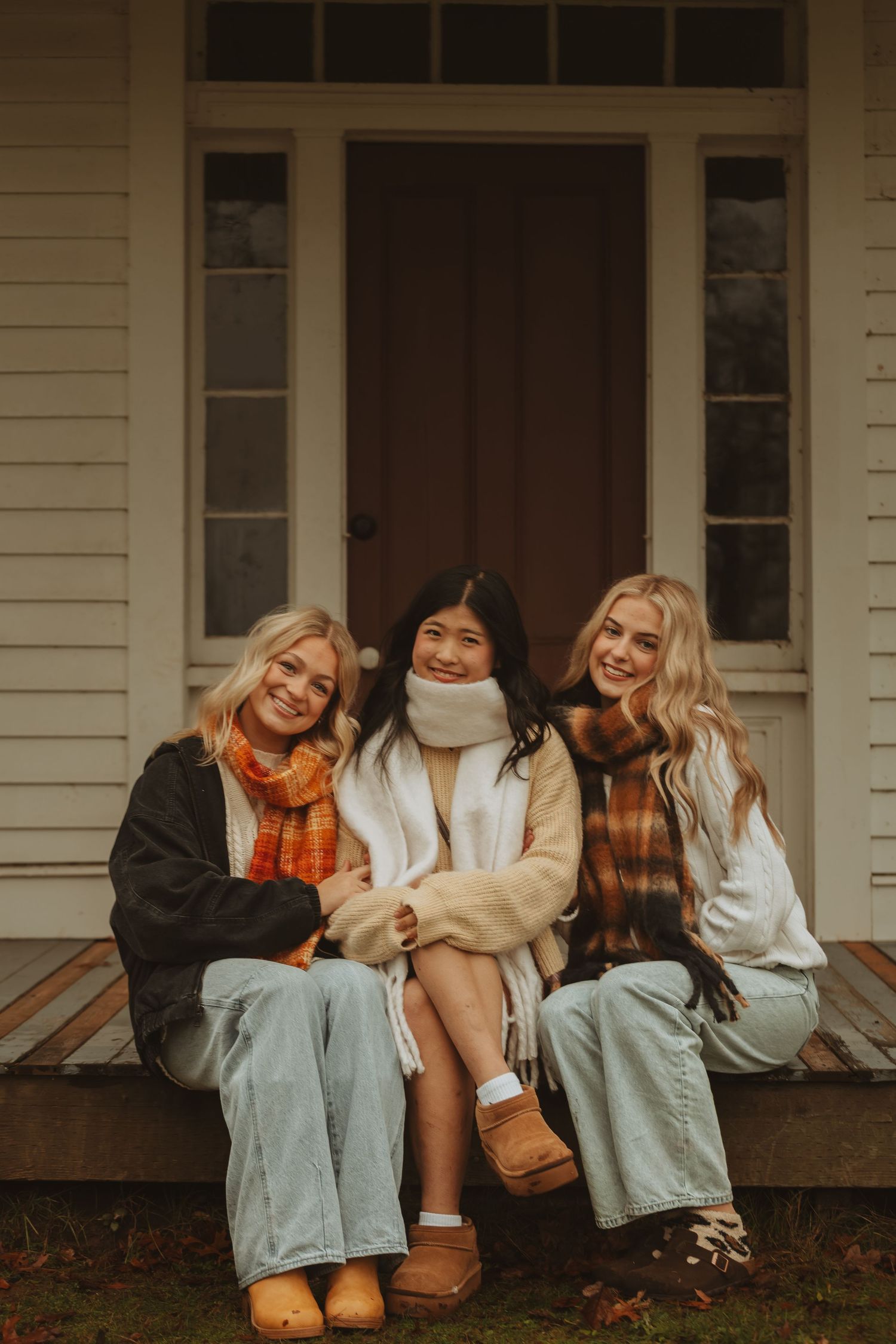 Friends lounging together on a rustic porch wearing fall clothing and sharing laughter in warm afternoon light.